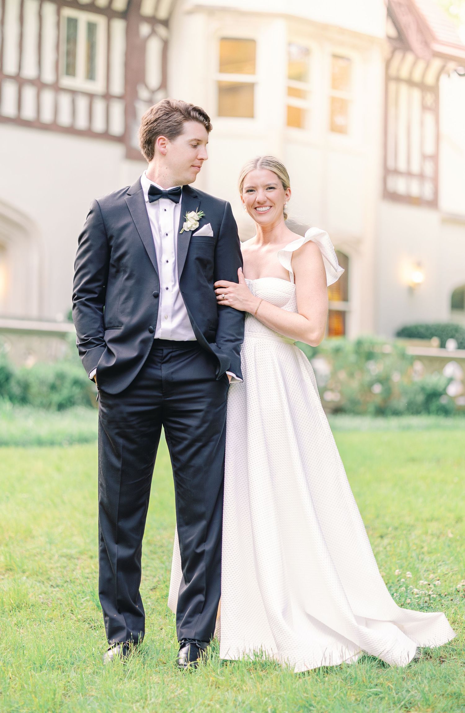 Romantic outdoor wedding portraits show bride and groom in formal attire posing playfully on a grassy lawn.