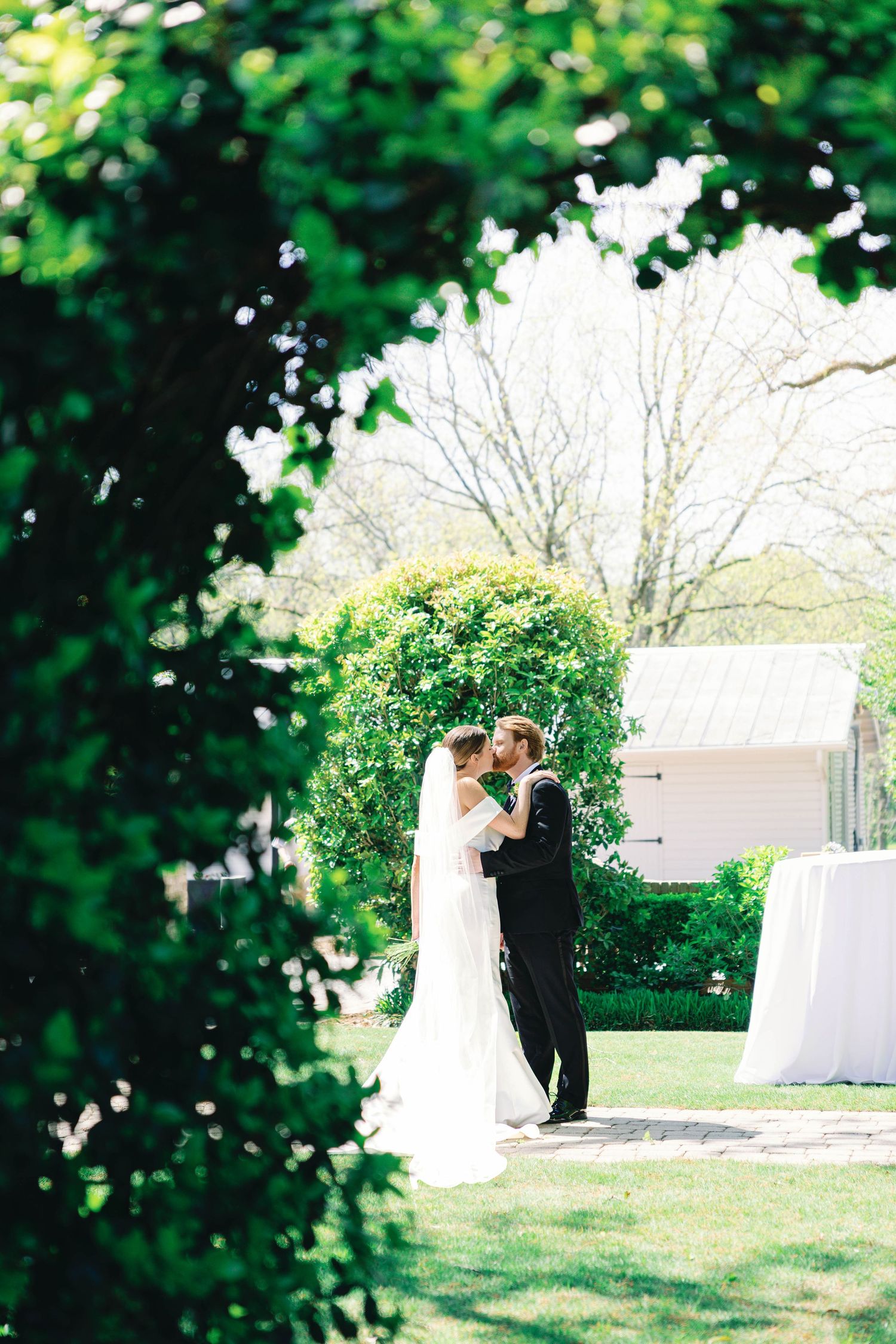 A wedding couple shares an intimate moment on a garden path framed by lush greenery.