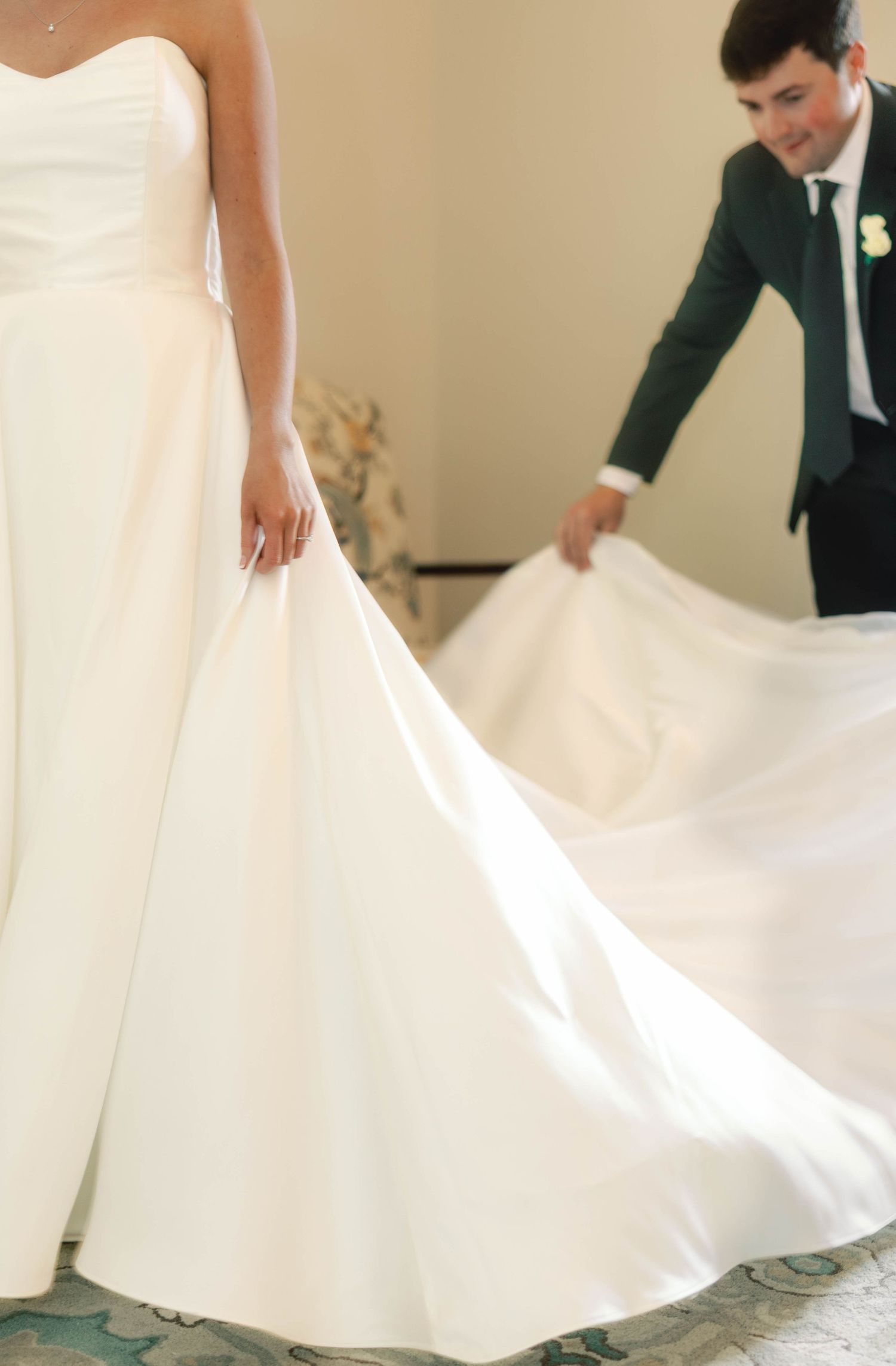 A close-up view of a flowing white wedding dress train being arranged on a patterned floor.