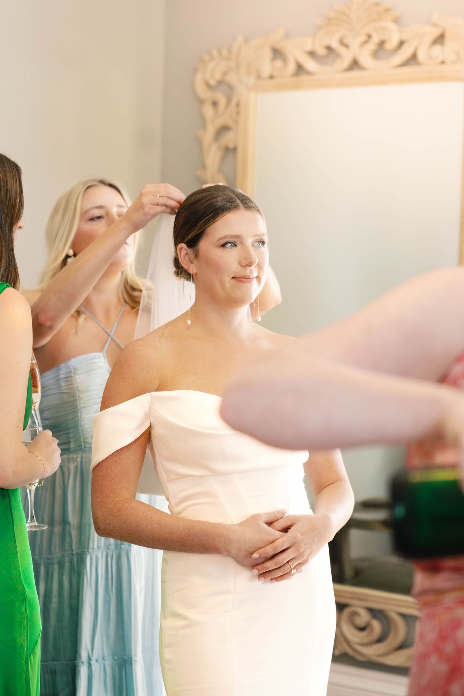 Getting ready scene with elegant white wedding dress in ornate mirror reflection.