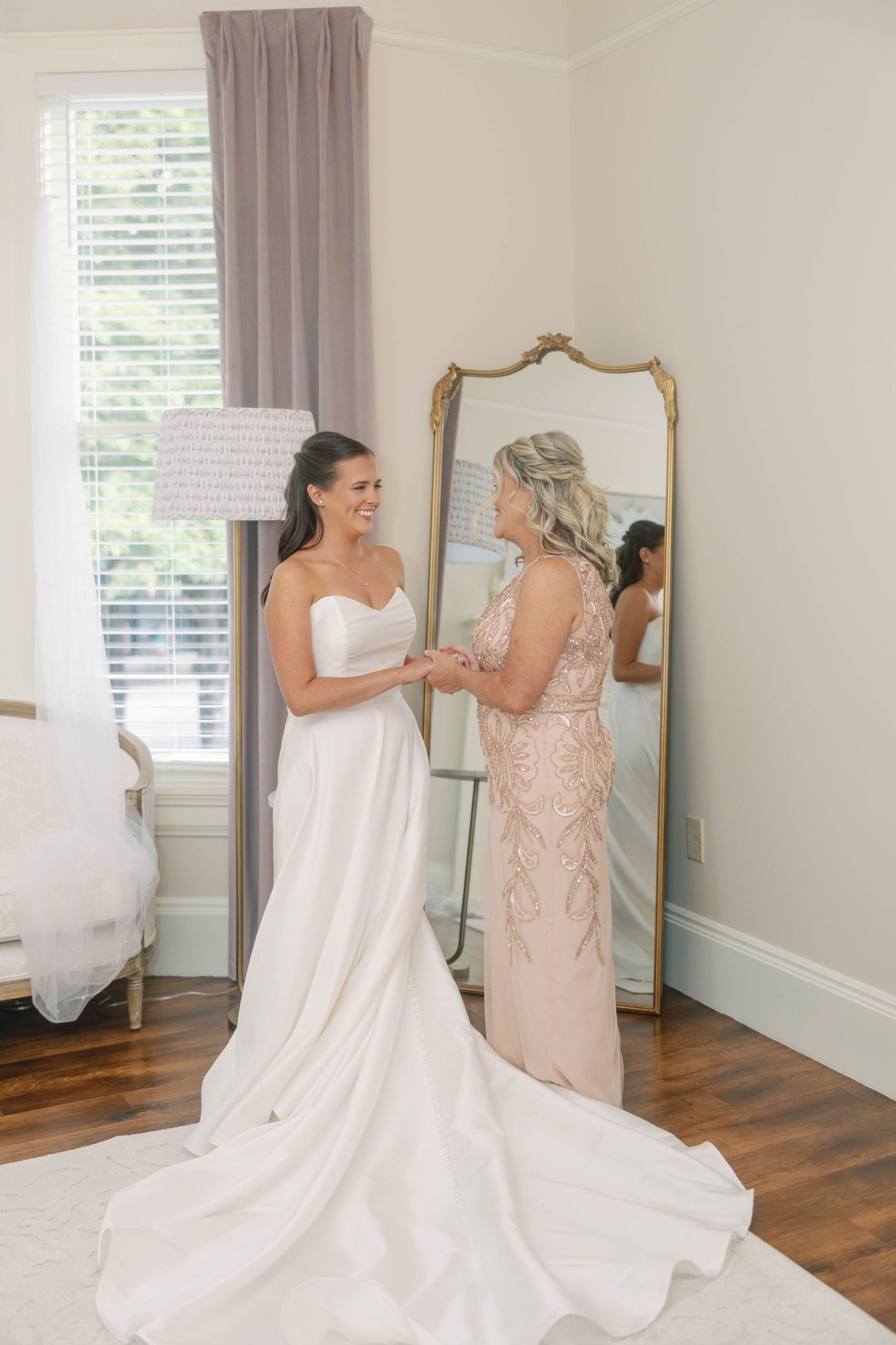 Wedding preparation scene showing a bride in her gown getting ready with help in a bright room with mirrors.