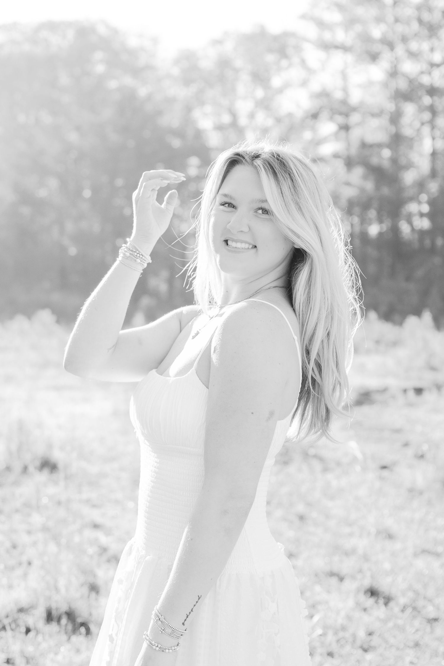 Woman in white dress poses playfully against sunlit natural backdrop.