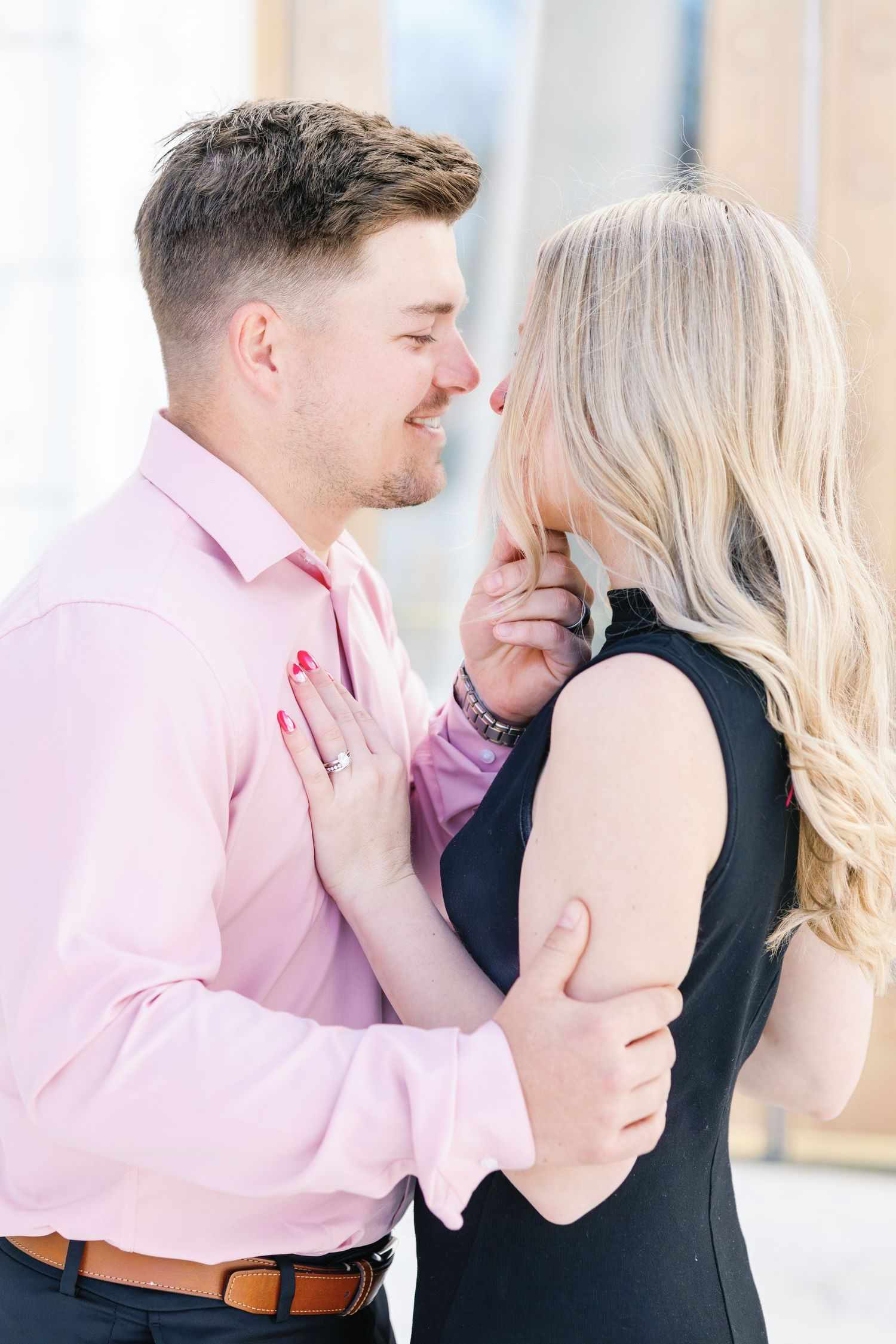 Intimate portrait of couple in pink shirt and black dress sharing tender moment outdoors.