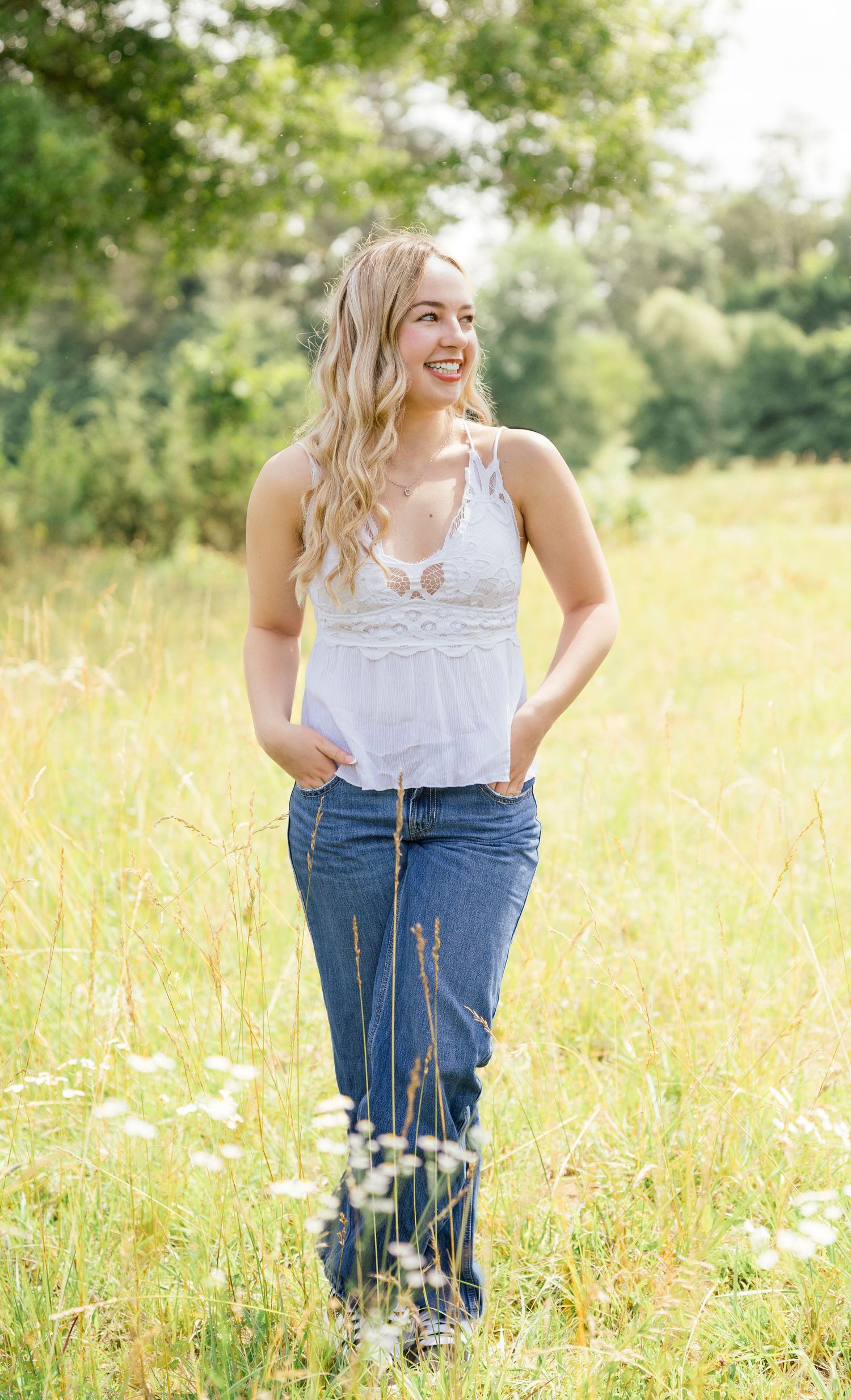 Four outdoor portraits in a sunny field with tall grass and daisies show someone in a white lace top and jeans.