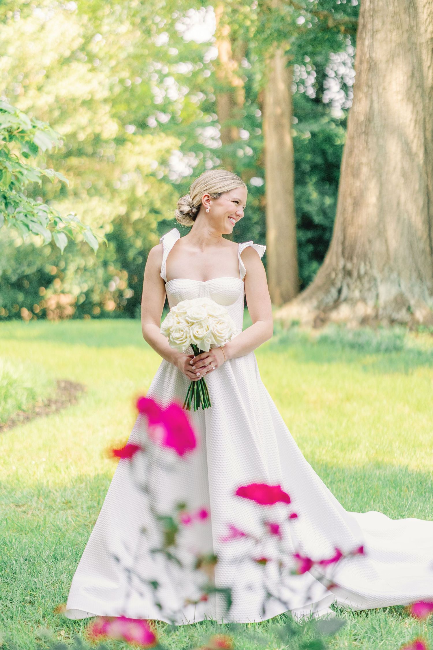 Elegant wedding gown with fluttering sleeves and white bouquet photographed in garden setting with pink florals.