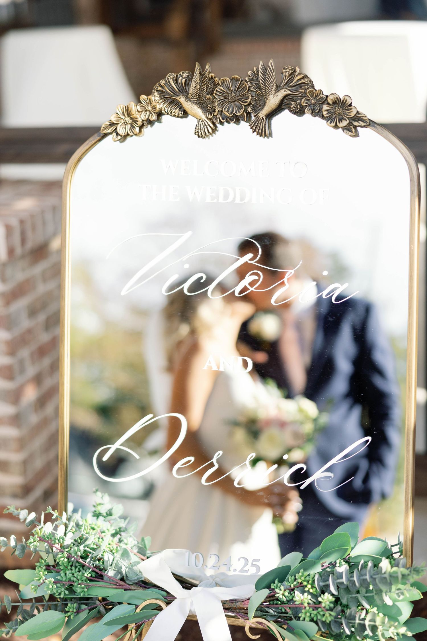 Elegant gold-framed mirror decorated with greenery and white calligraphy for a romantic wedding reception setup.