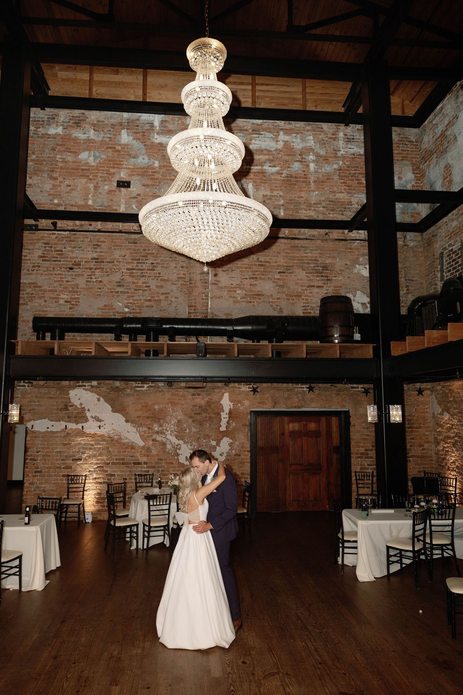 Wedding venue with elegant crystal chandeliers and exposed brick walls featuring hardwood dance floor.