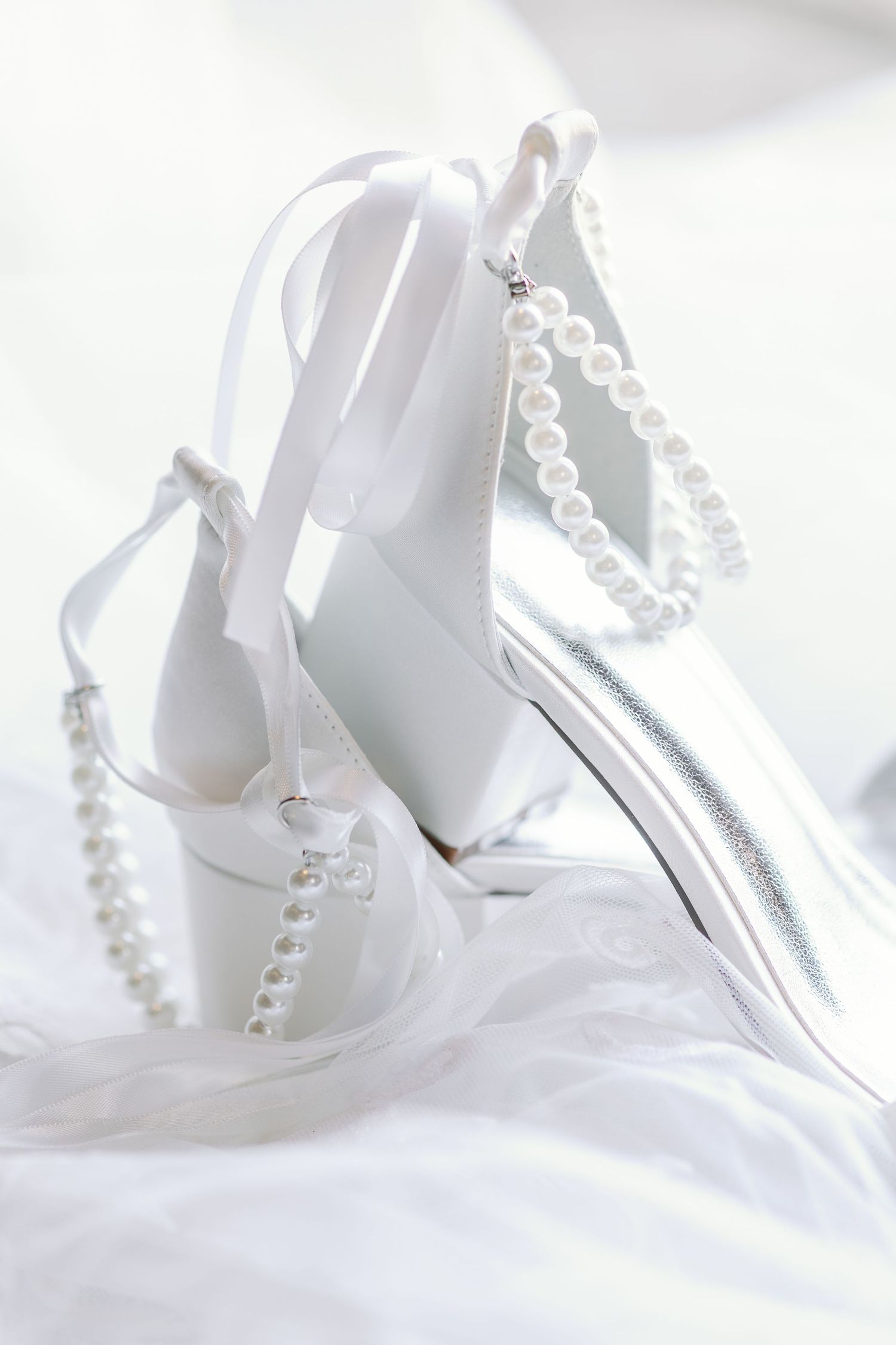 White bridal heels with pearl straps displayed on soft white fabric.