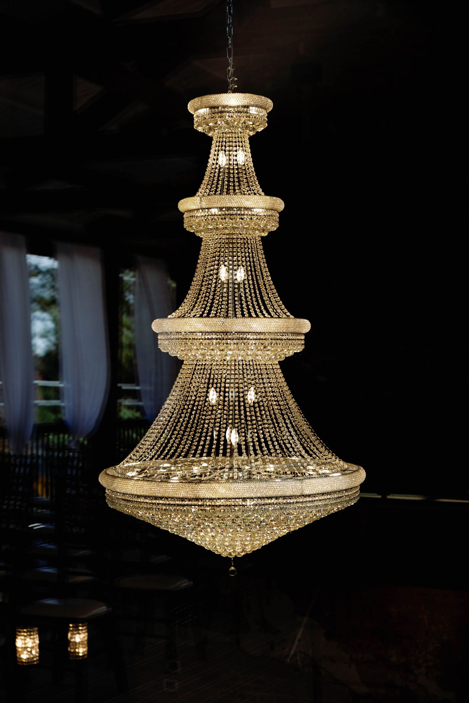 Elegant tiered crystal chandelier with cascading beads and multiple levels glowing warmly in a dark room.
