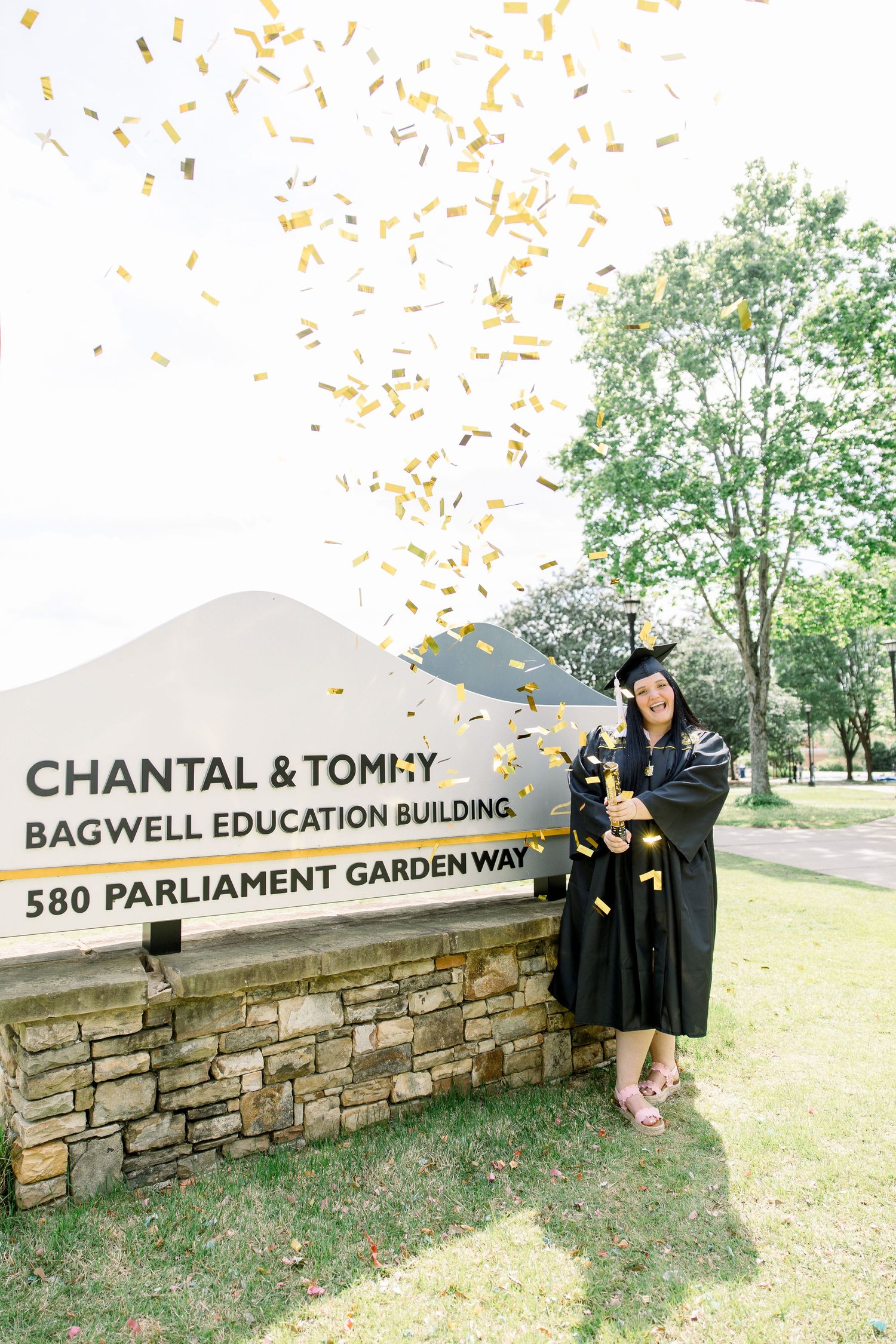 Graduates celebrate with confetti at Bagwell Education Building sign.