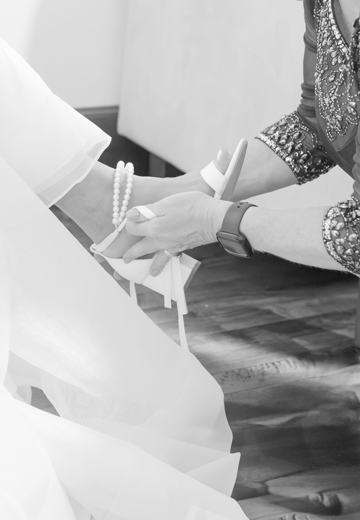 Black and white photo of hands adjusting pearls and gloves during wedding preparation.