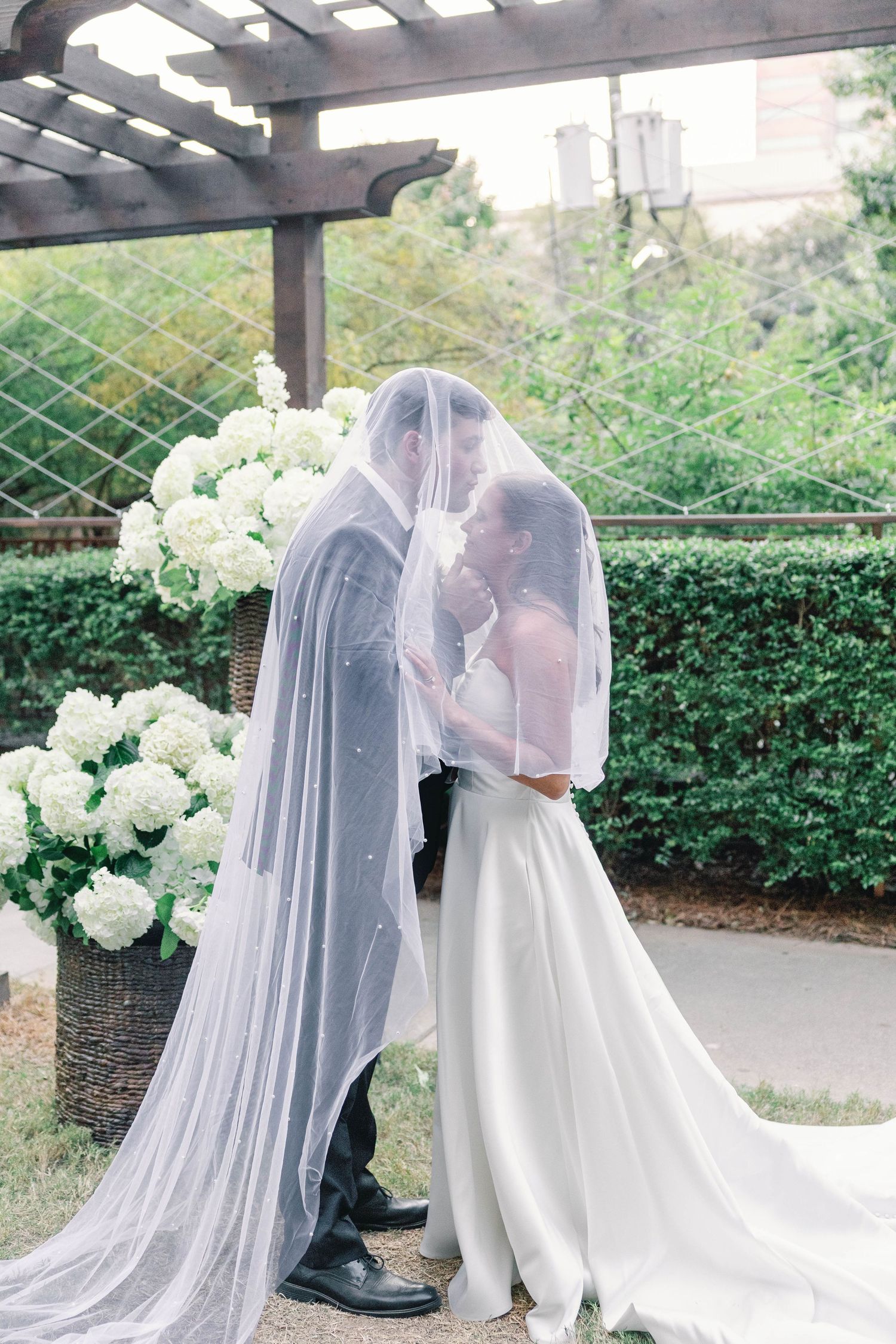 Romantic wedding couple sharing an intimate moment under a covered walkway with white hydrangeas and greenery.