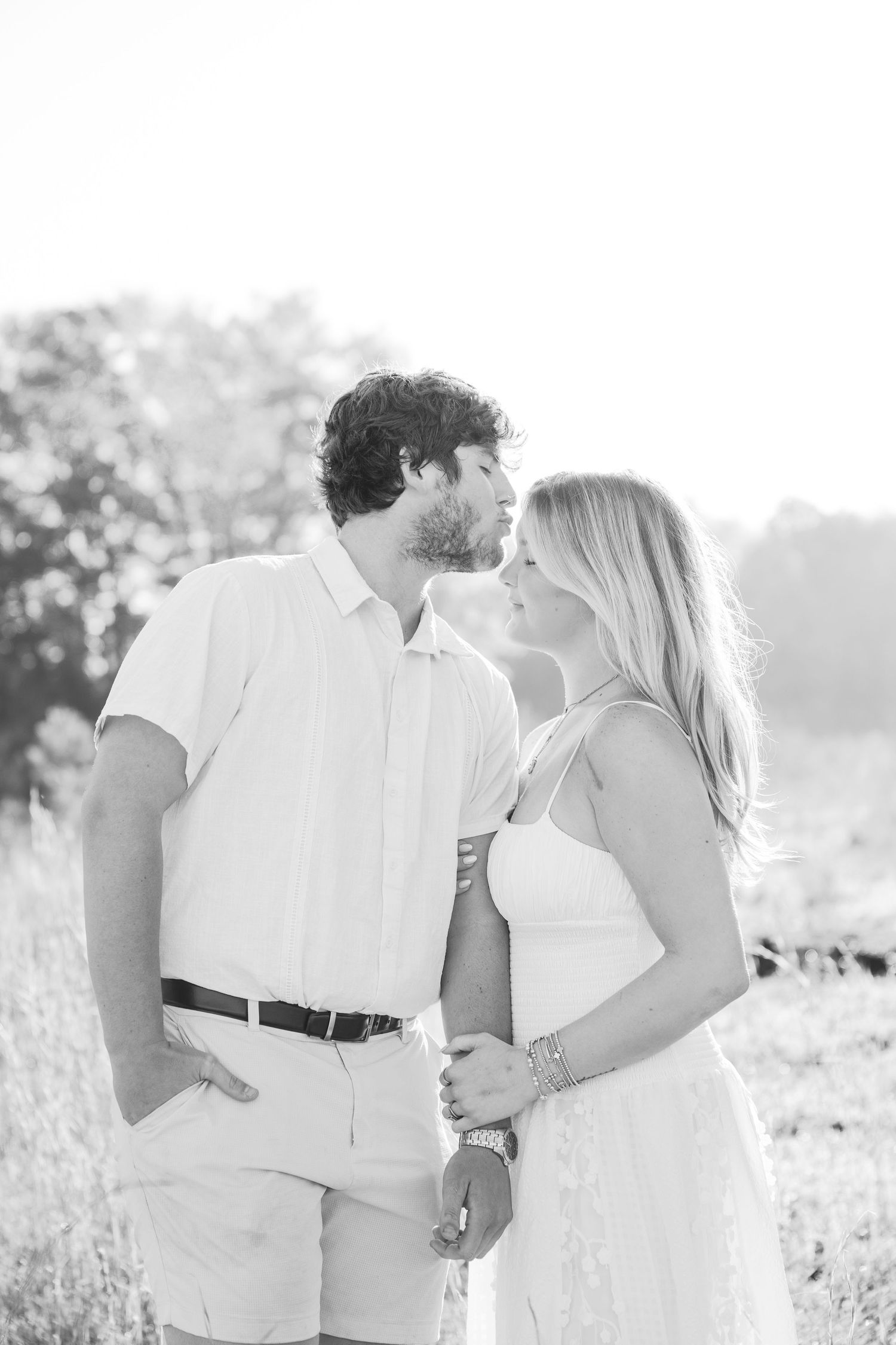 Black and white portrait of couple in white clothing sharing intimate moment in sunny field.