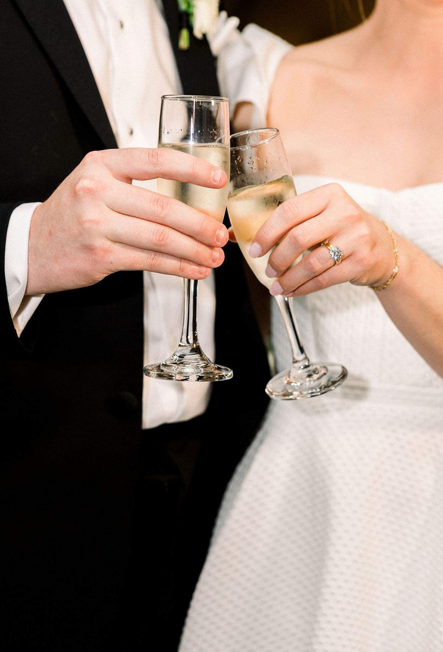 Two hands clink champagne glasses together in celebration during a formal wedding reception.