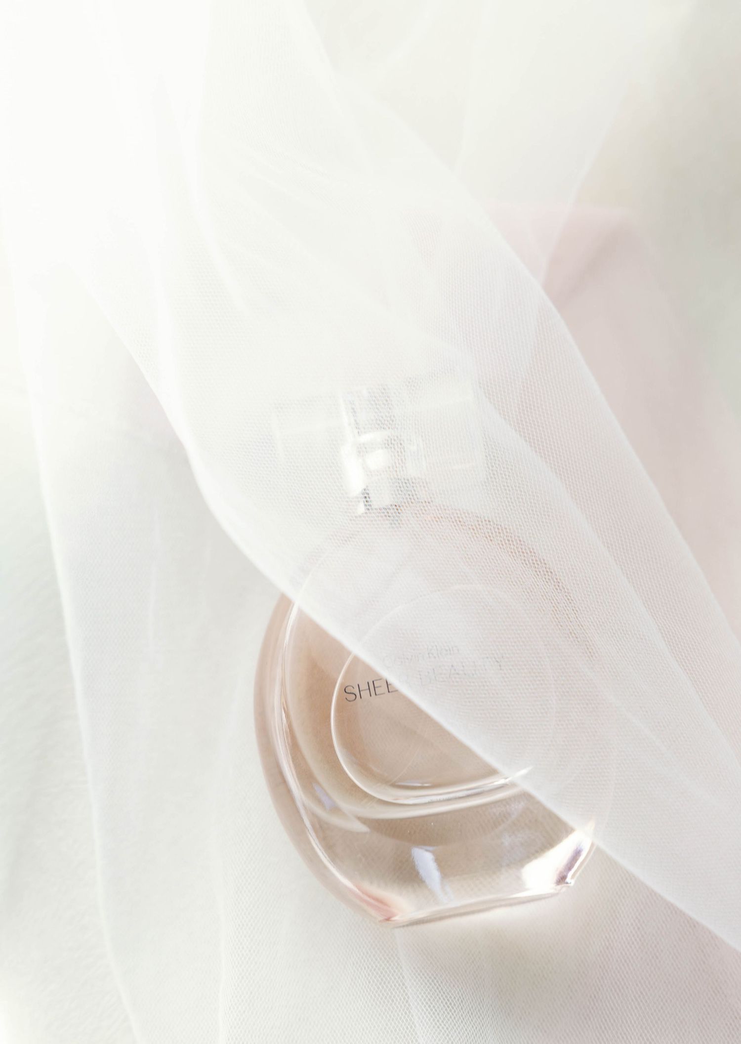 A delicate white veil draped over a rose gold wedding ring against a soft pale background.