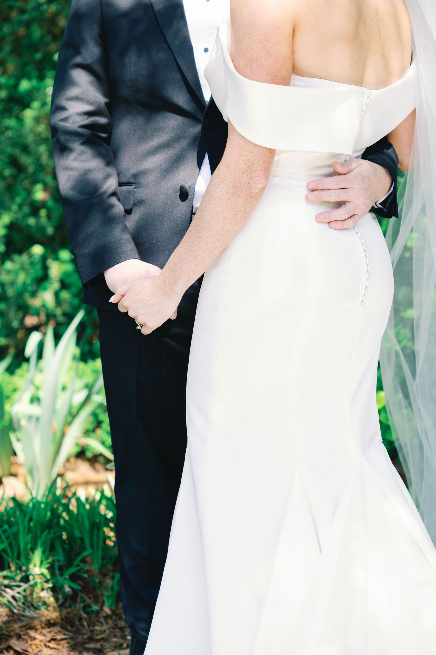 Detail shot of wedding couple embracing showing elegant white dress and black tuxedo.