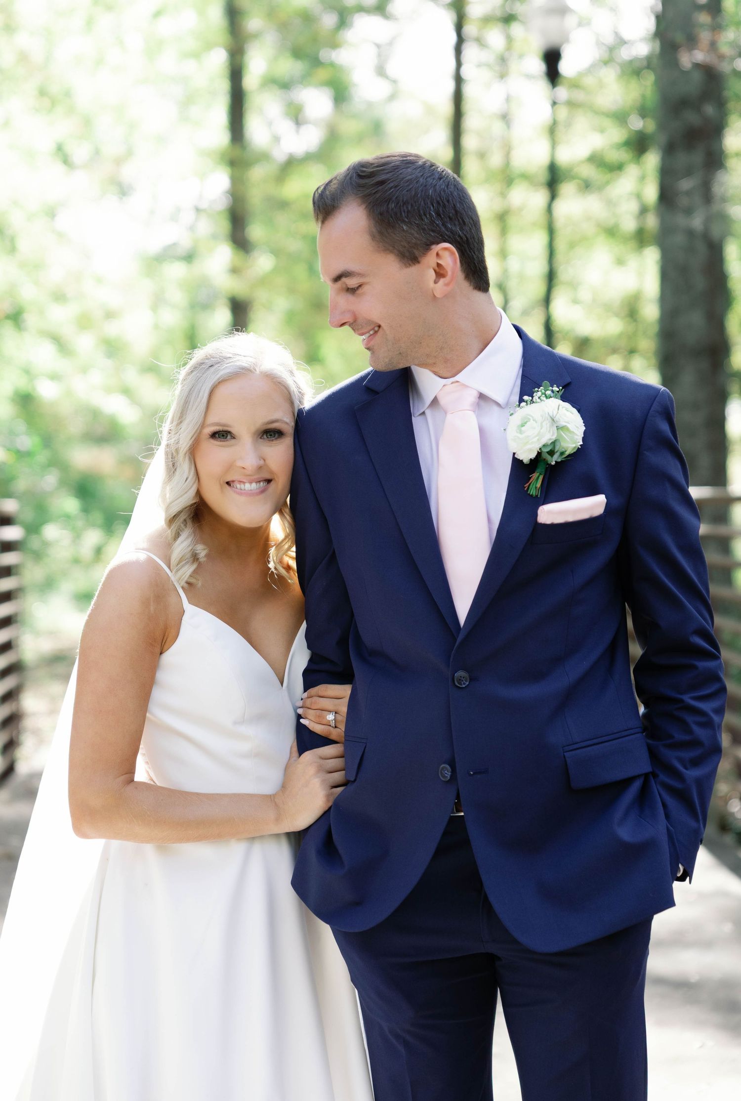 A couple in wedding attire share intimate moments while walking through a wooded outdoor setting.