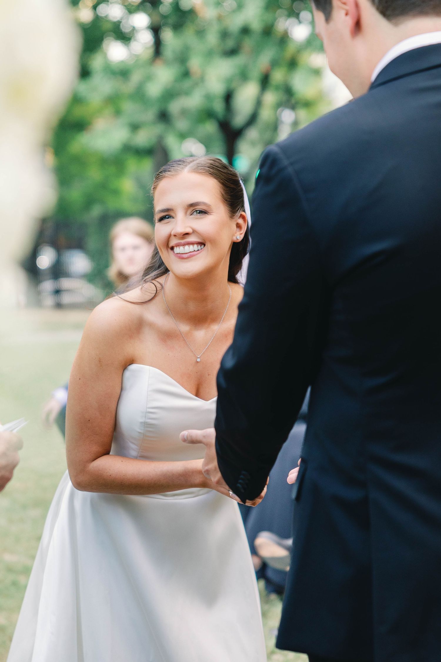 A joyful outdoor wedding ceremony shows a couple exchanging vows surrounded by greenery and natural light.