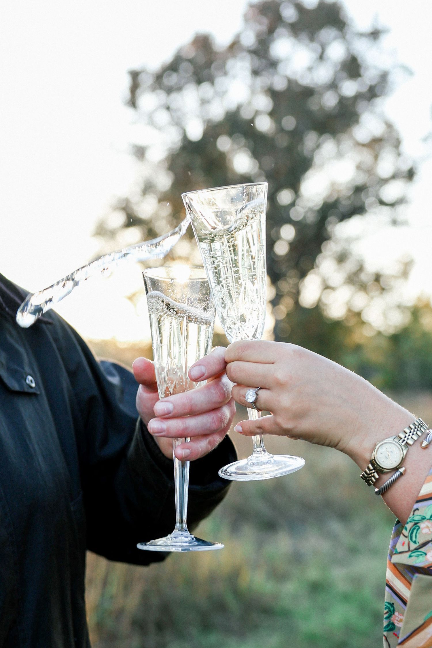 Close-up view of crystal champagne glasses clinking together in celebration at an outdoor event.