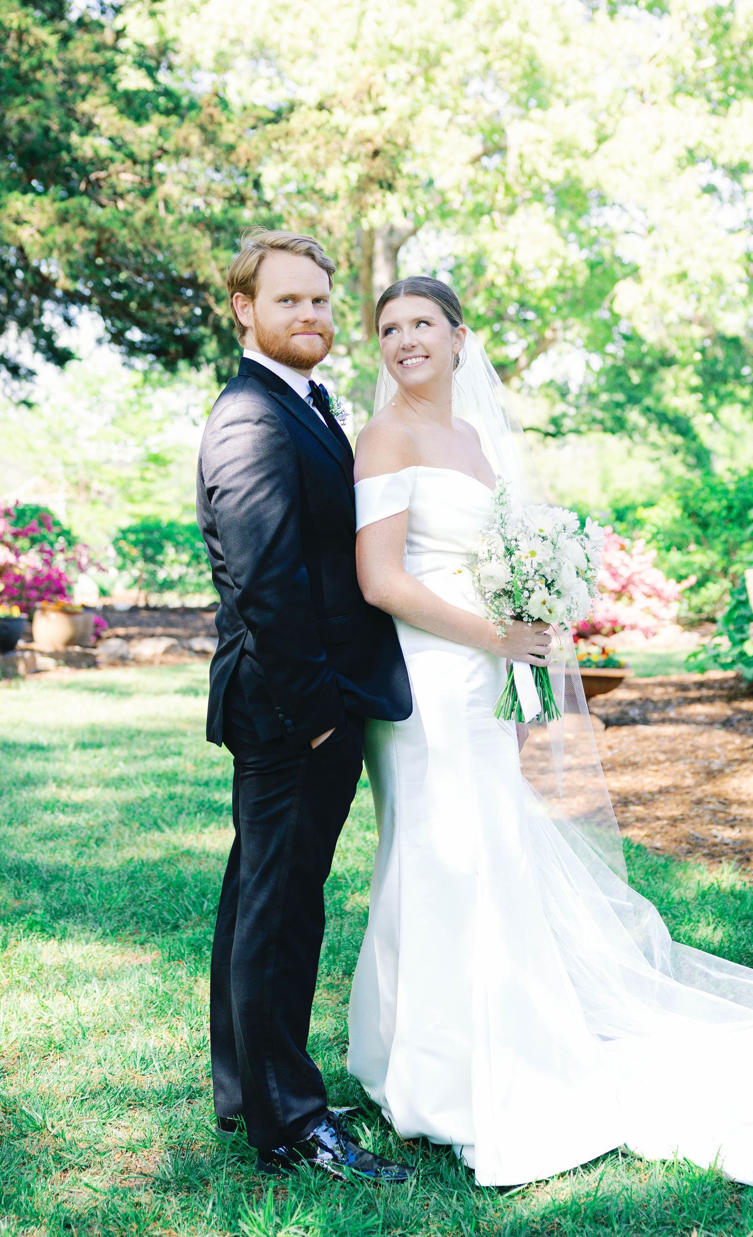 Wedding couple poses together on garden lawn with blooming azaleas in background.