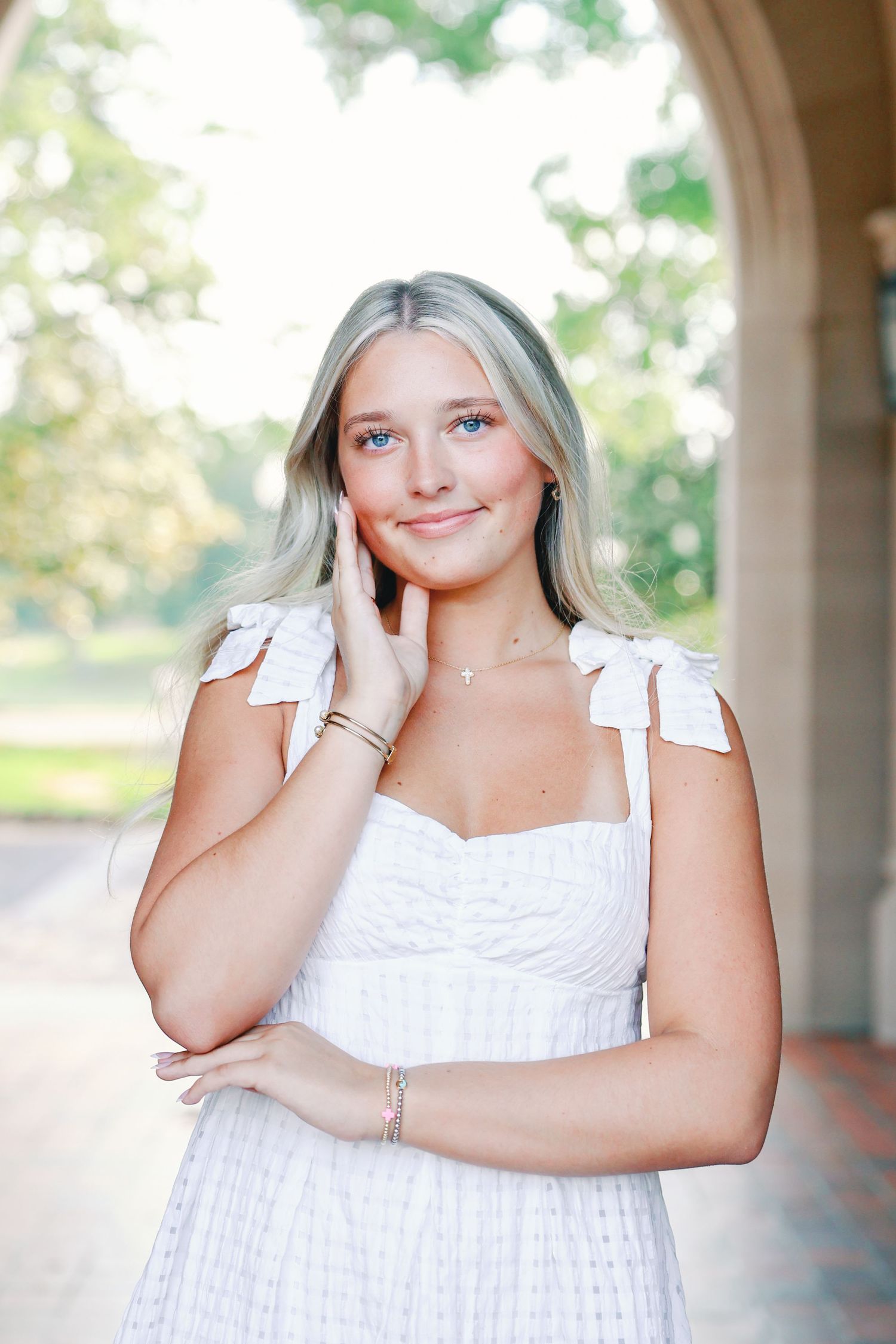 Portrait of someone in a white summer dress with flutter cap sleeves posing against an outdoor architectural background.