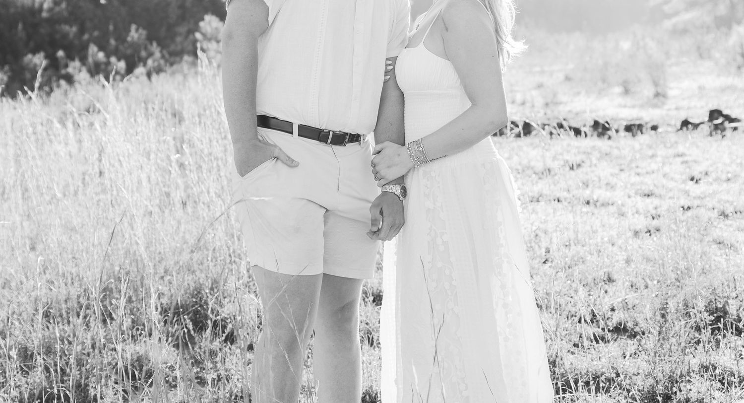 Romantic couple posing together in a sunny field wearing light summer attire.