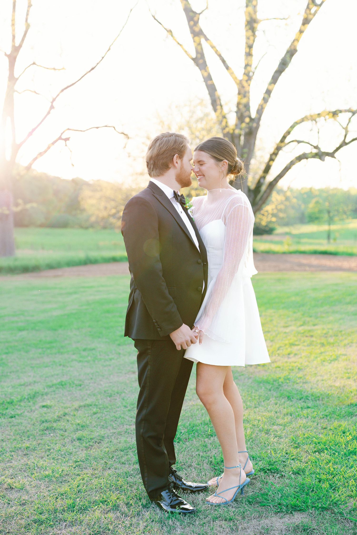 A romantic moment captured between two people in formal wear under a sunlit tree.