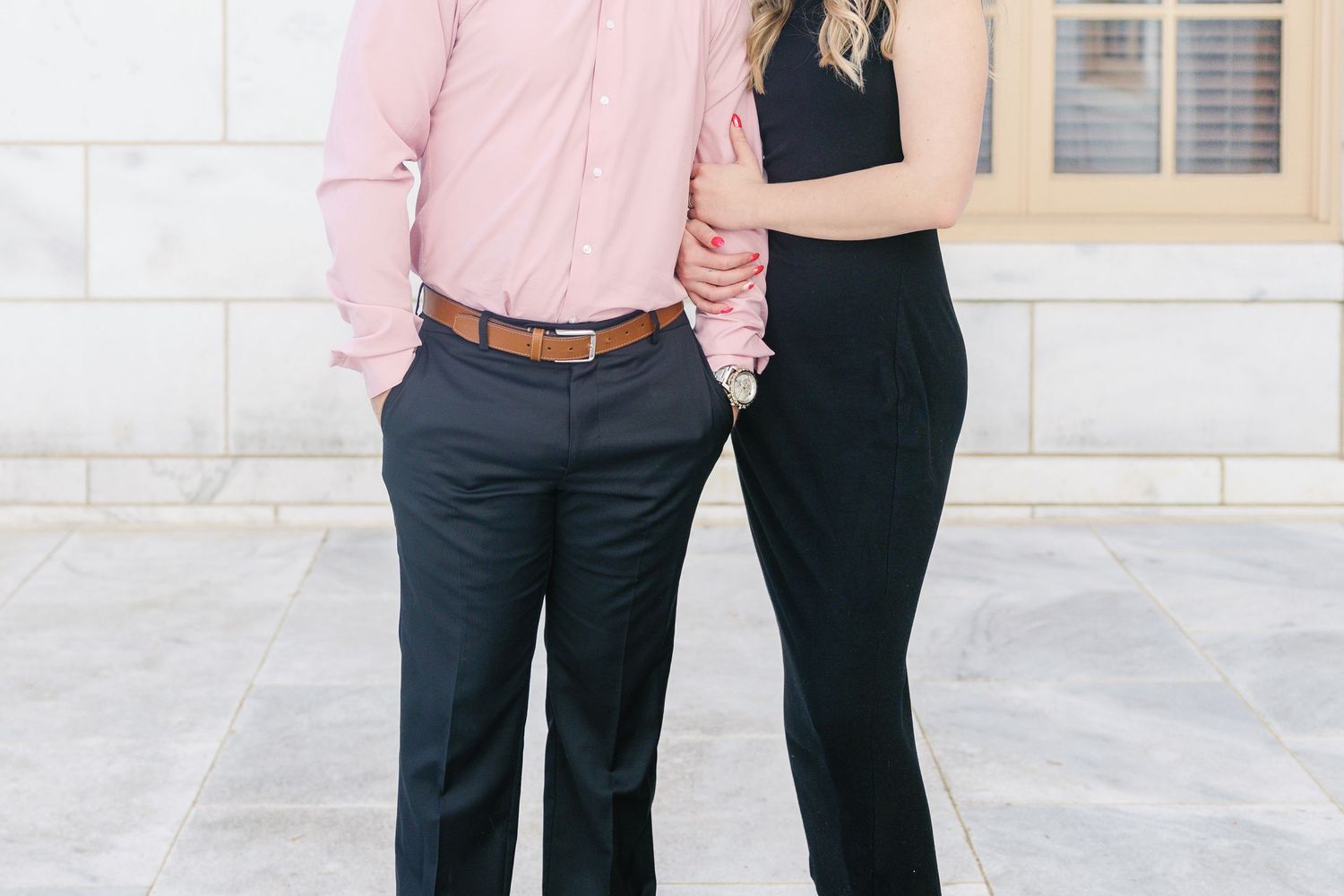 Couple in coordinated black and pink outfits stand close together against white stone wall.