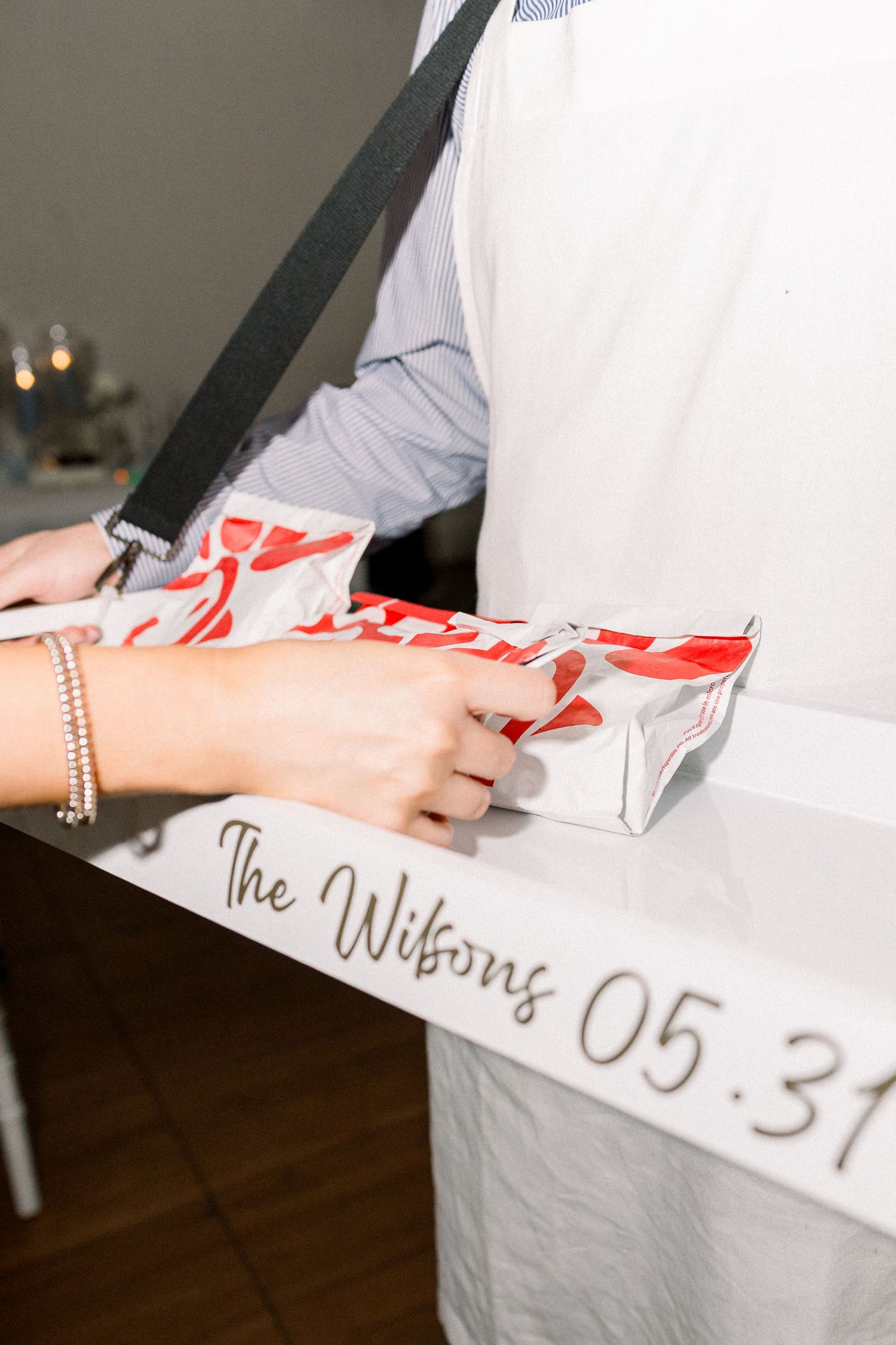Hand signing a white tablecloth with markers next to silver and red gift wrapping materials at an event.