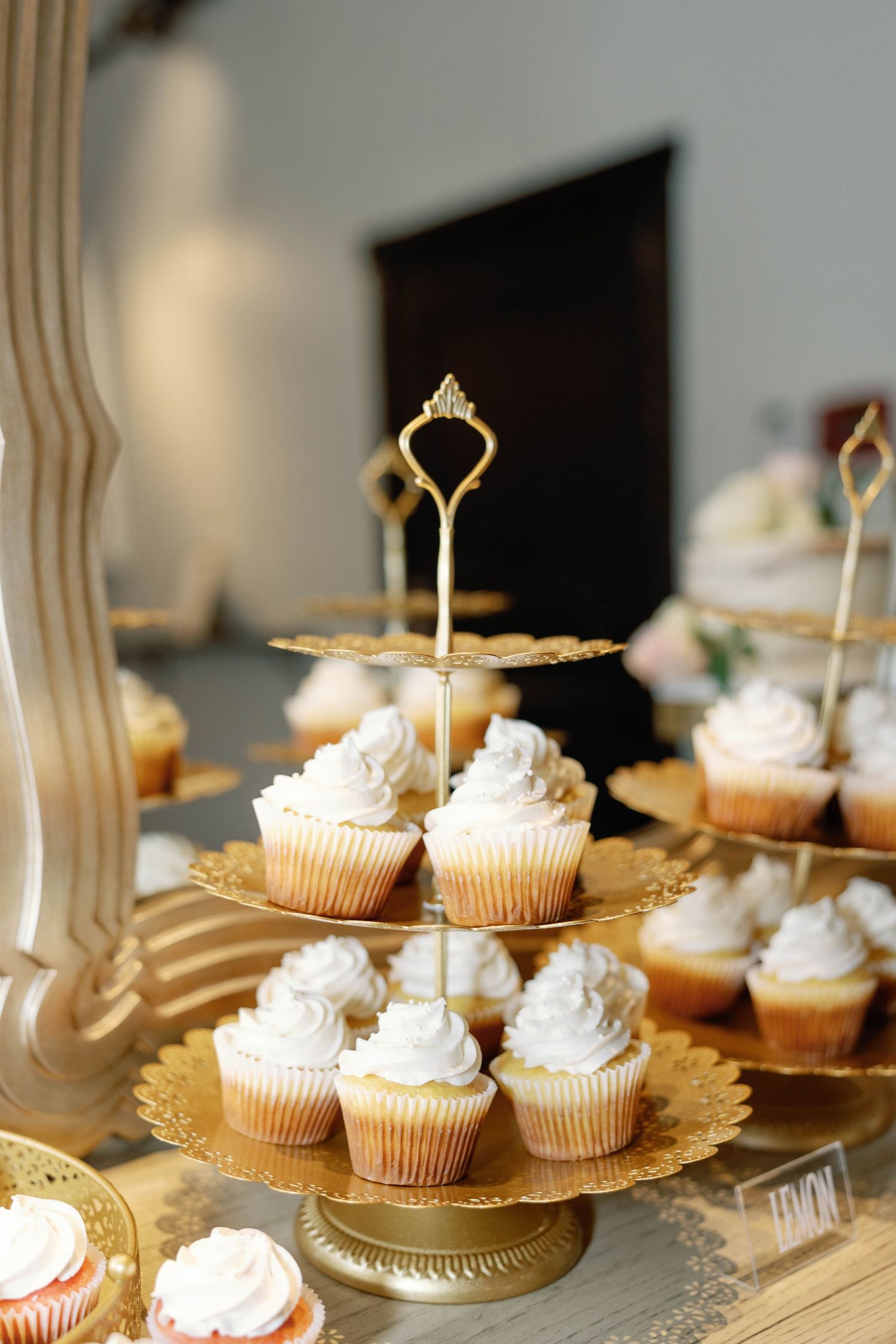 White frosted cupcakes with gold decorative toppers arranged on an elegant gold doily platter for a special occasion.