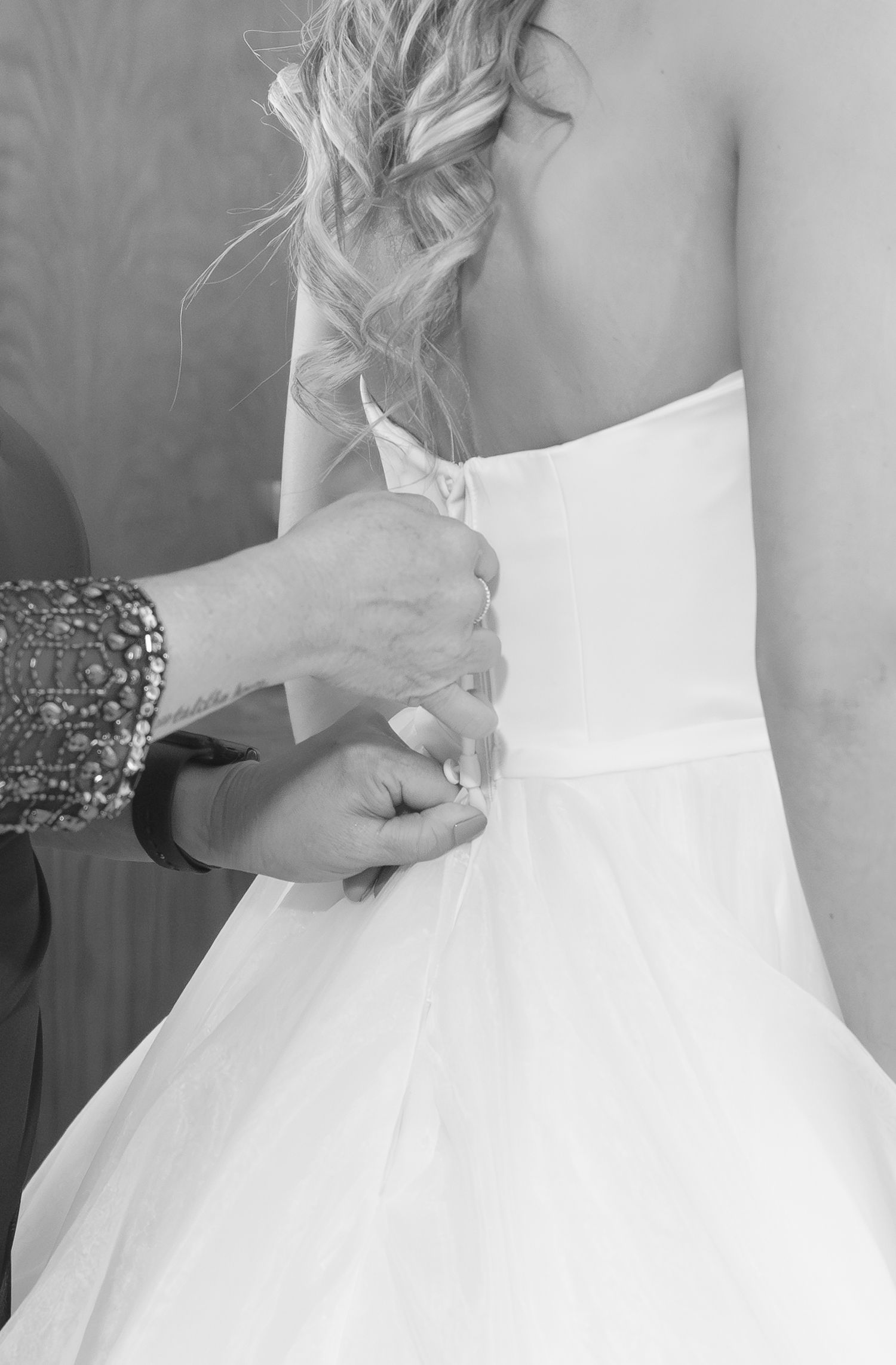 Close-up of hands adjusting the back of a white wedding dress.