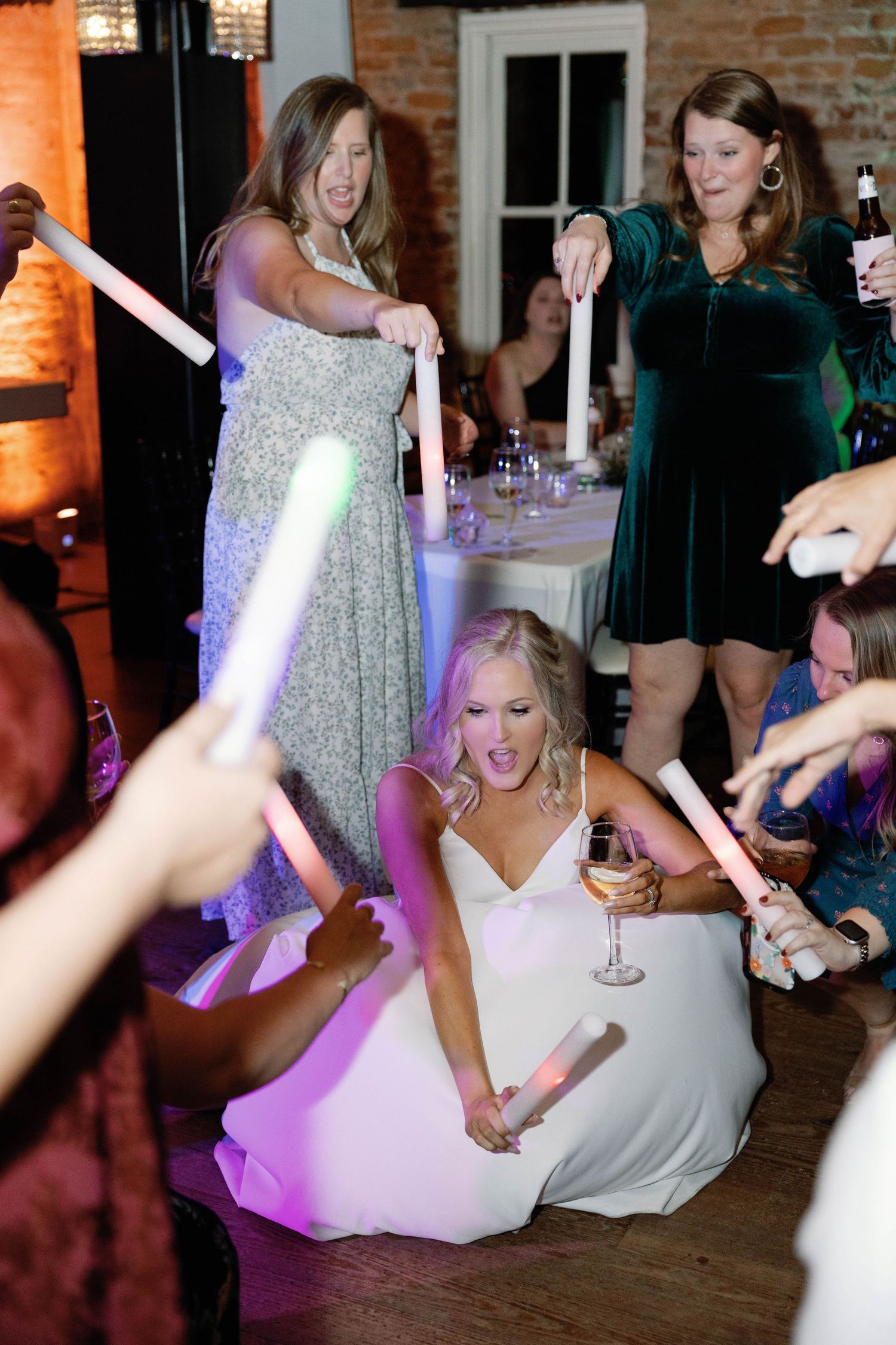 Dance party at wedding reception with colorful purple lighting and guests celebrating on dance floor.