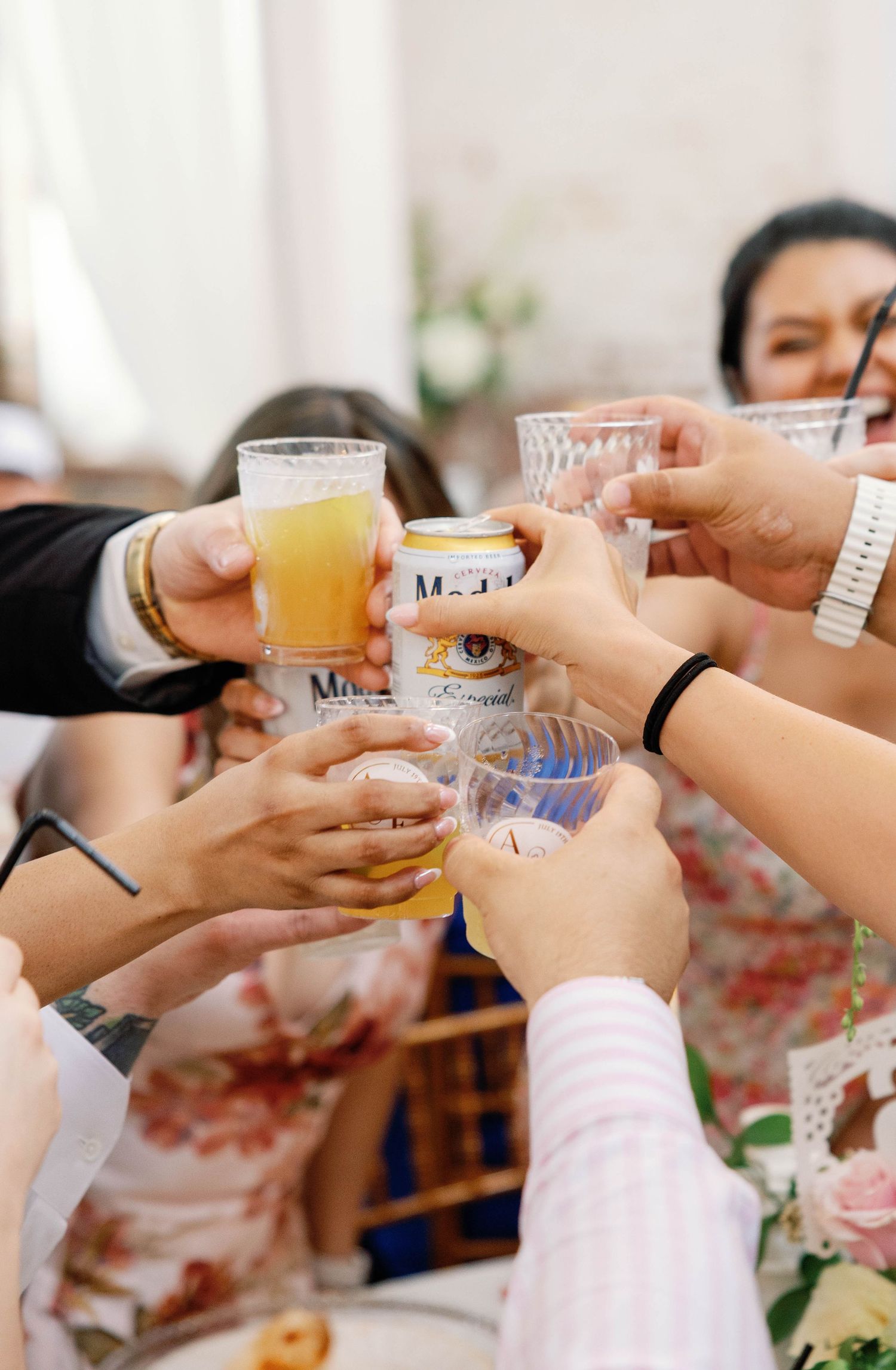 Hands reach across a table to cheers with small shot glasses filled with colorful drinks.