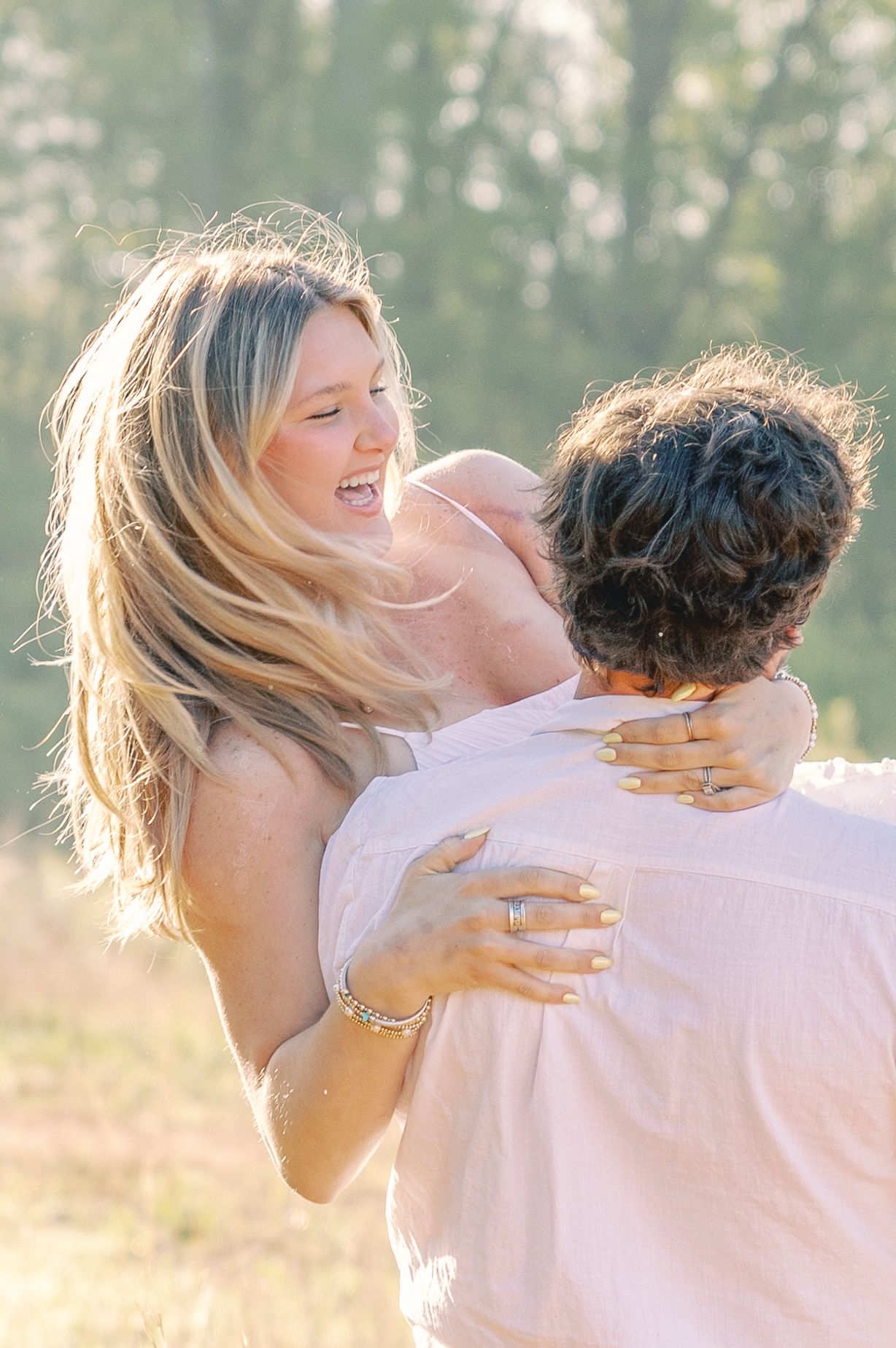 Couple sharing playful moment in sunlit field with flowing hair and natural expressions.