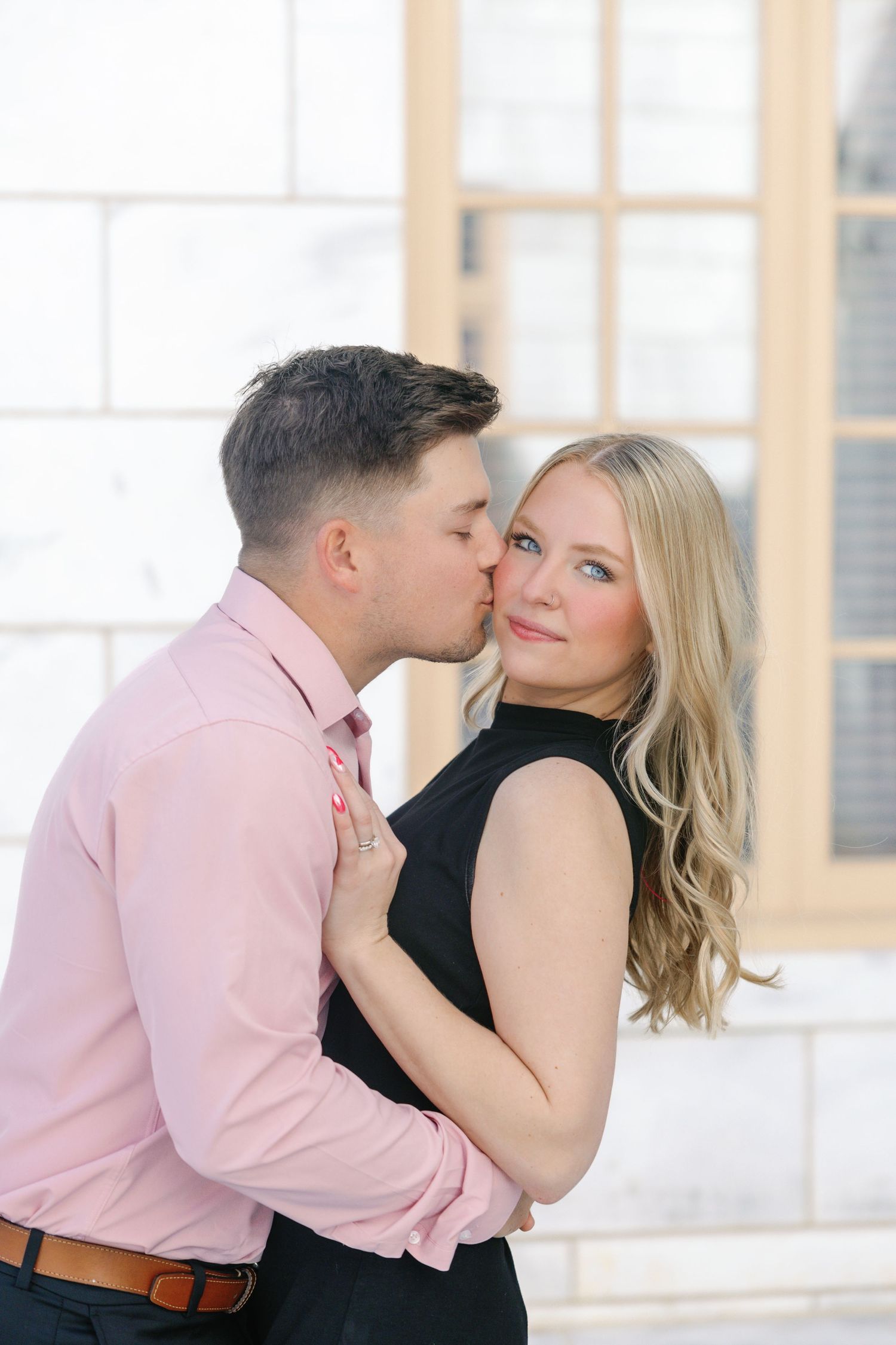 Romantic portrait against white stone building with pink and black attire.