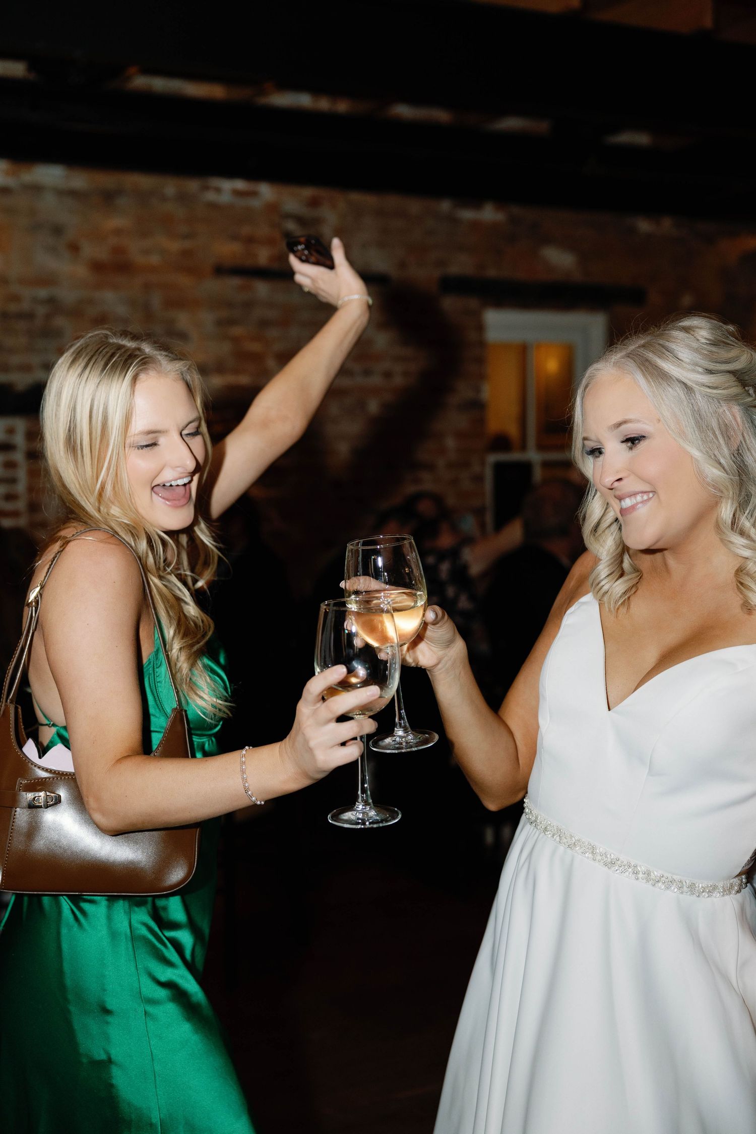 A group of friends in green and white dresses laugh and share drinks at a celebration.