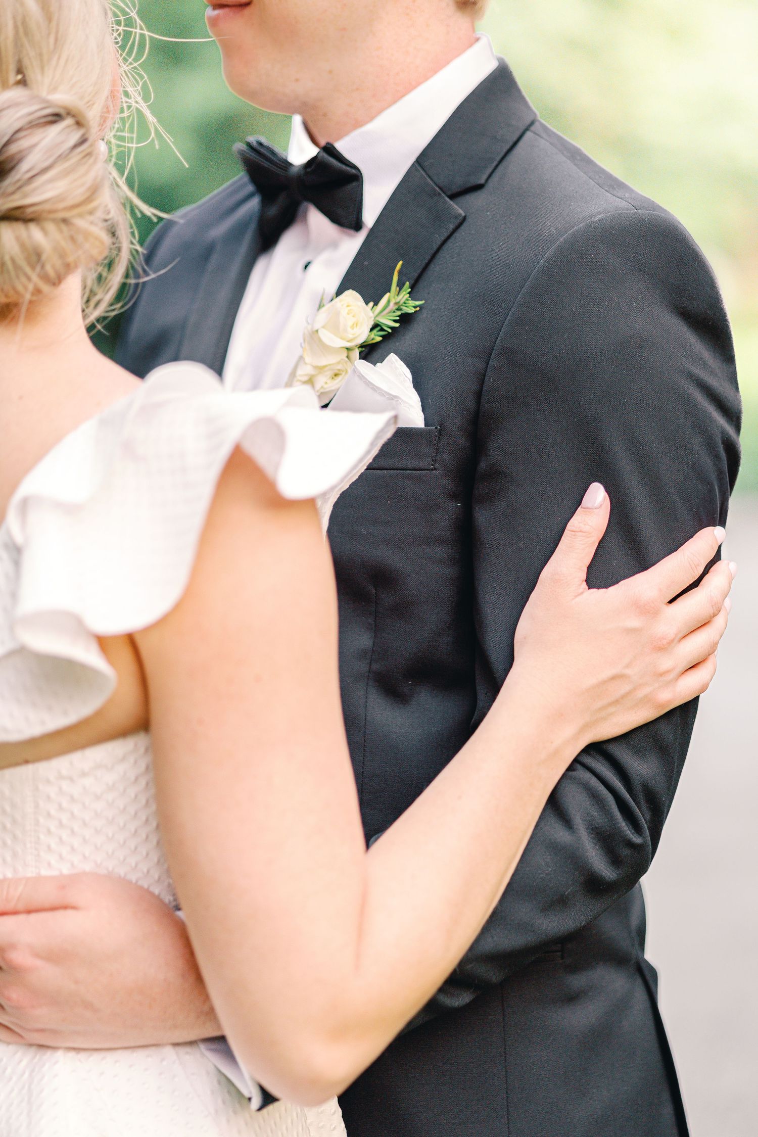 Close-up of a couple embracing at a wedding with a white dress and black tuxedo with bow tie and boutonniere.