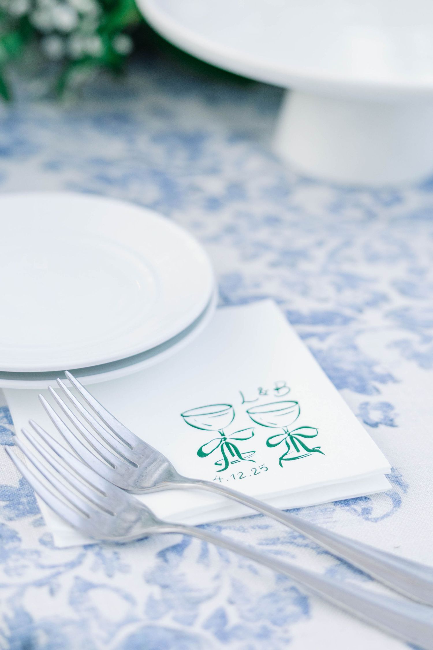 Wedding place setting with white plates and green champagne glass illustration on blue patterned cloth.