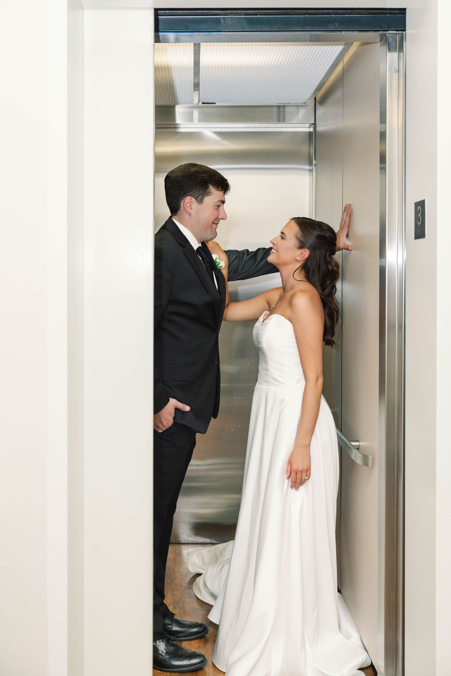 A bride and groom playfully interact in an elevator during their wedding photoshoot.