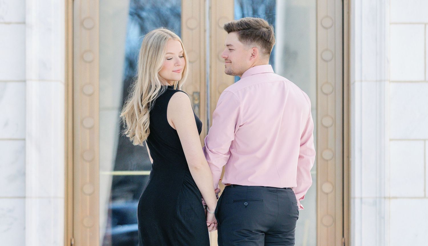 Couple in complementary outfits pose romantically by elegant doorway with decorative details.