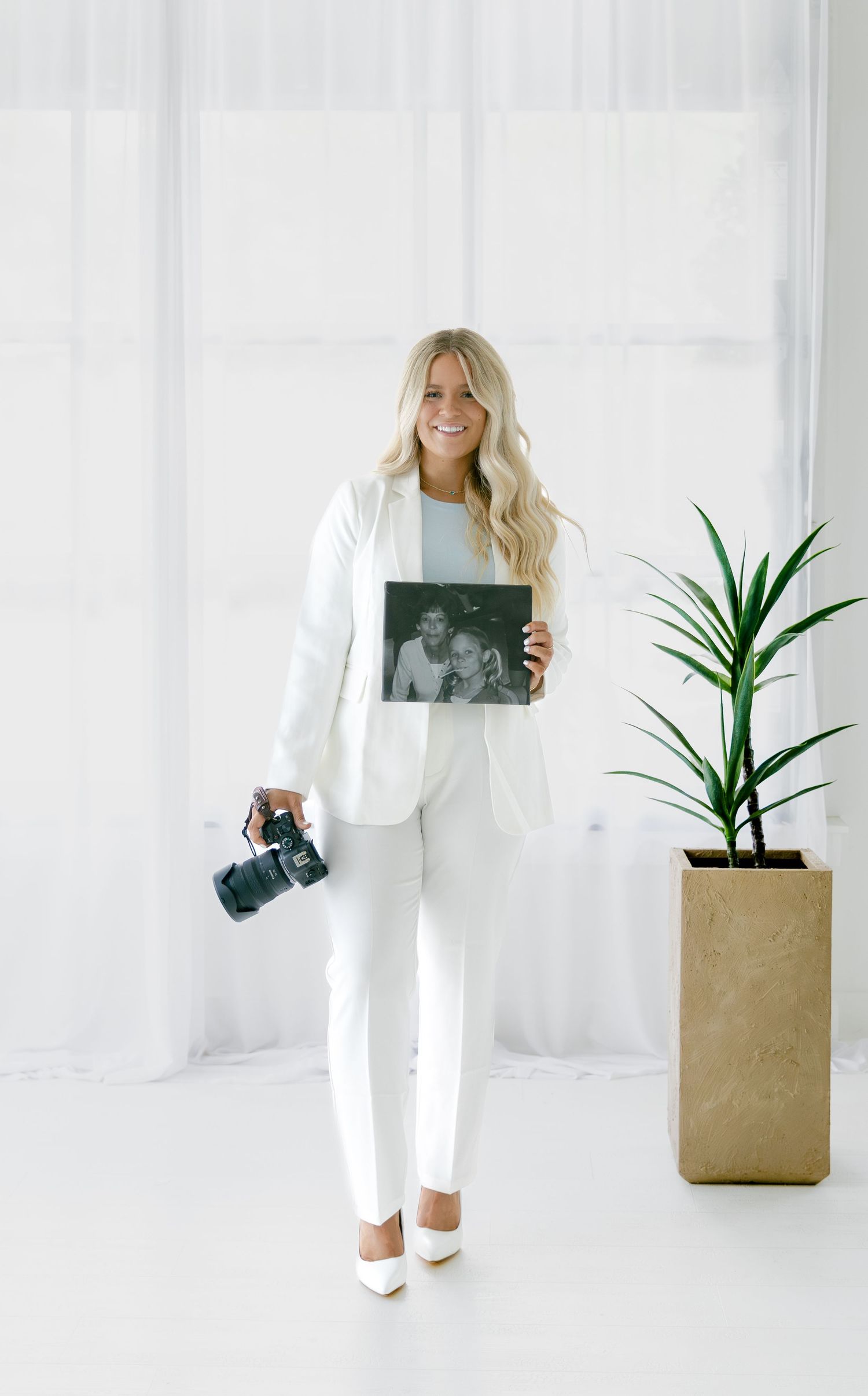 Photographer in all-white outfit holding camera and black and white photo print.