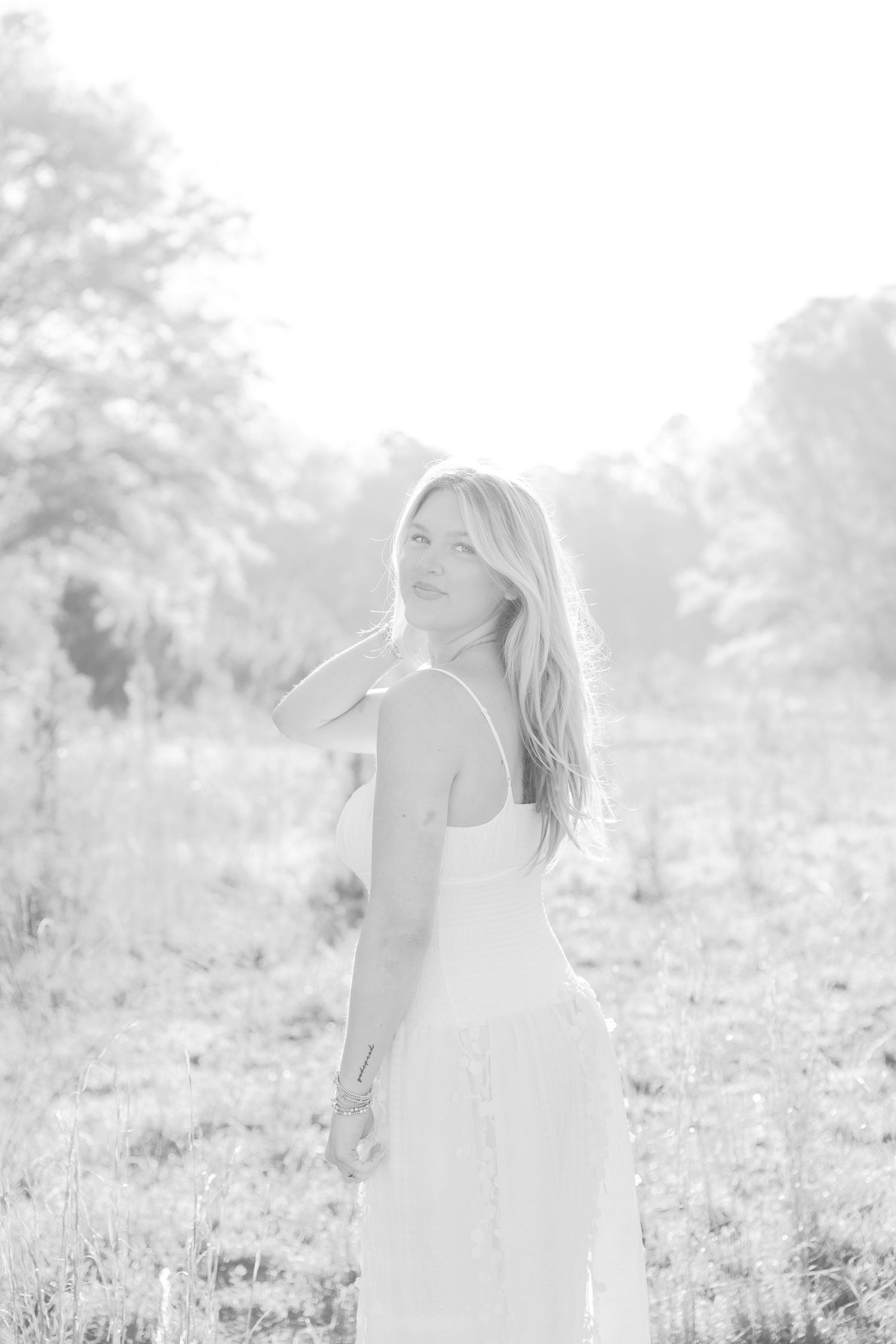 Ethereal black and white photo of a woman in white dress standing in a meadow.