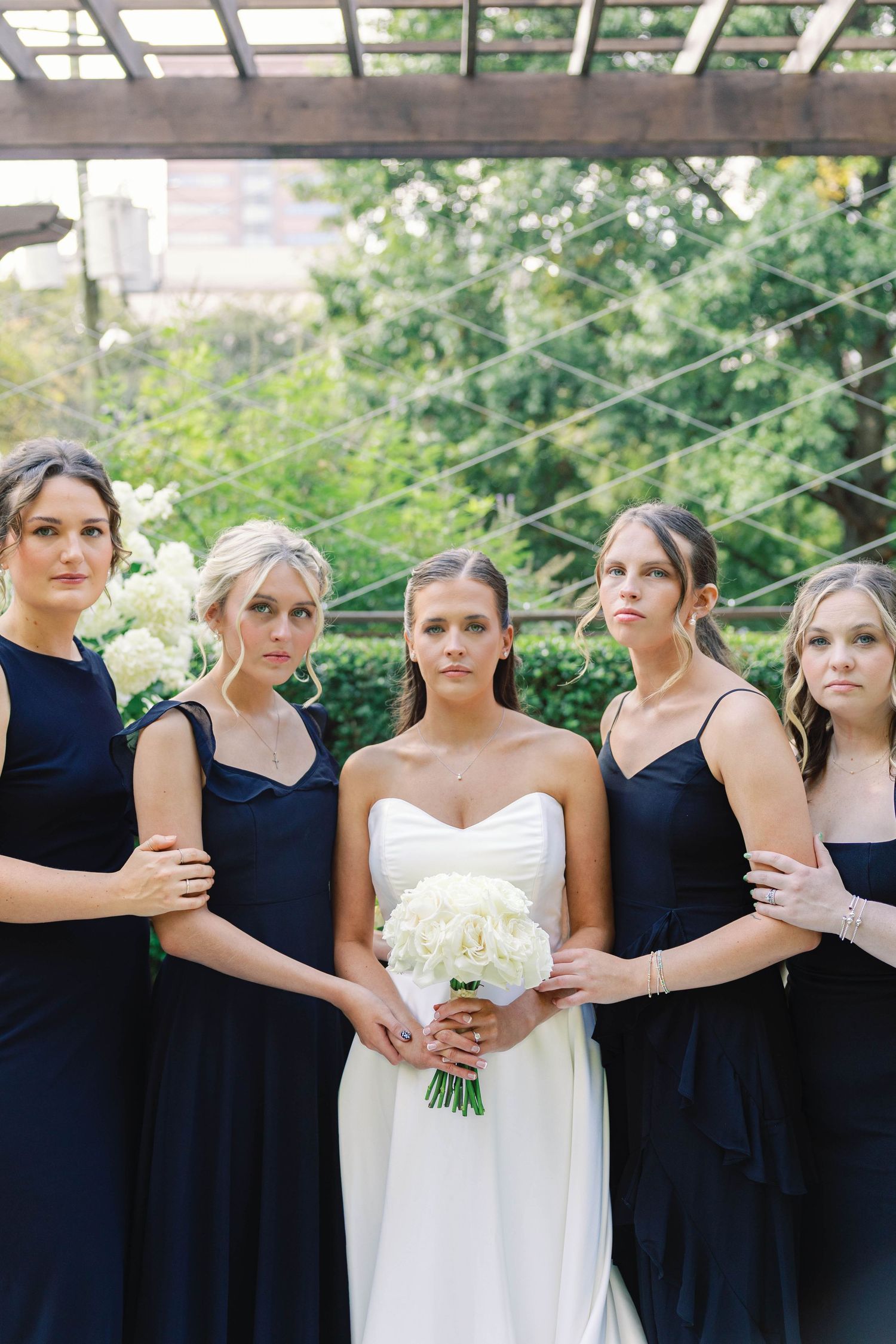 Bridal party in navy blue dresses and white bouquets posed together outdoors.