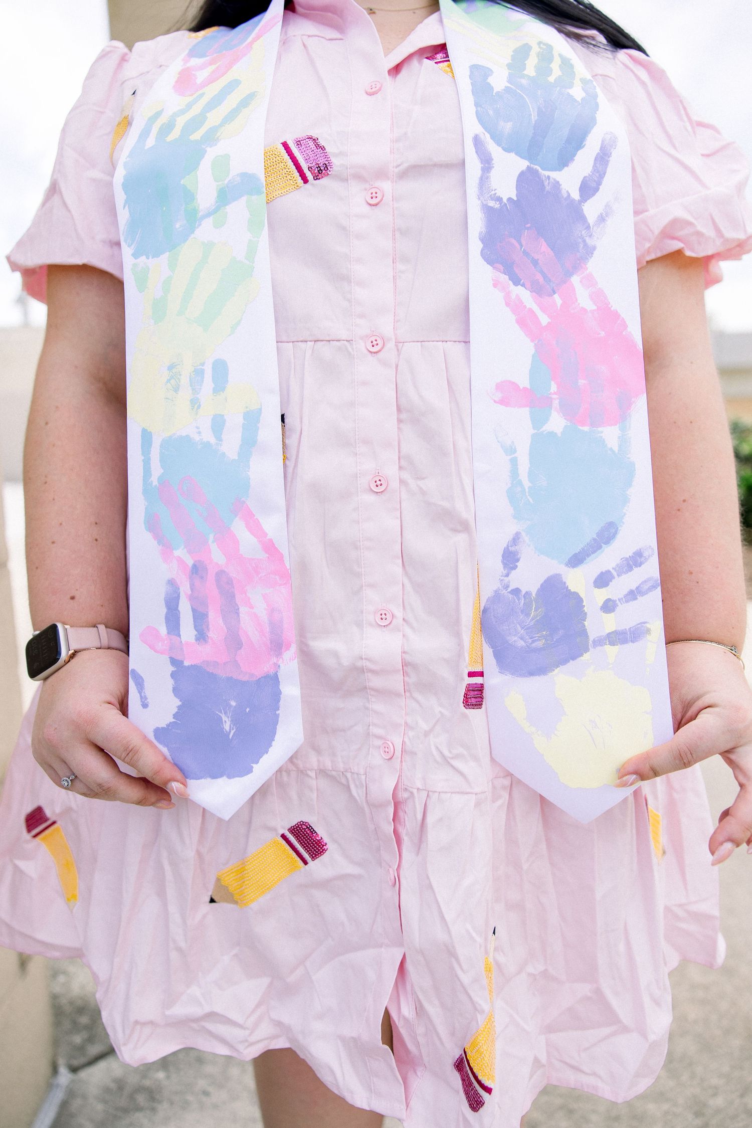 Close-up of pink dress with colorful handprint pattern and pencil decorations.