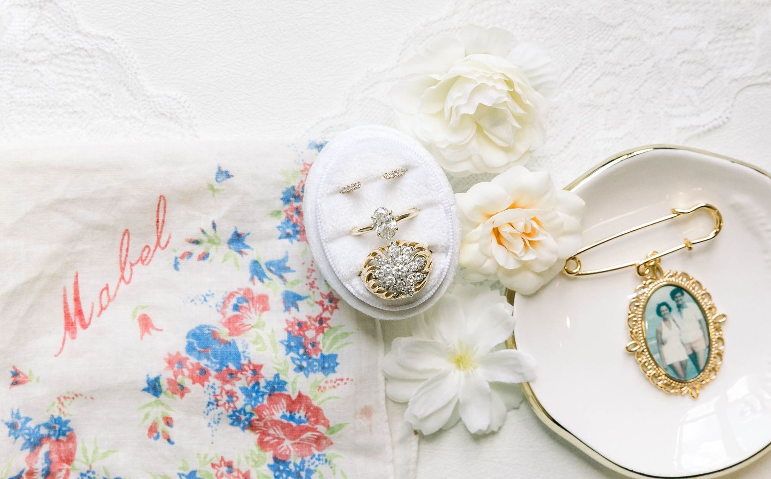 Feminine flatlay featuring vintage jewelry, floral fabric, and delicate white flowers on a light background.