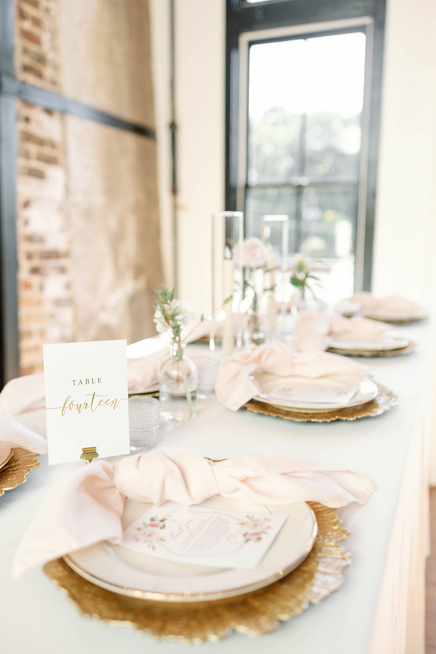 Elegant place settings with blush pink napkins and gold charger plates on a white tablecloth for a formal event.