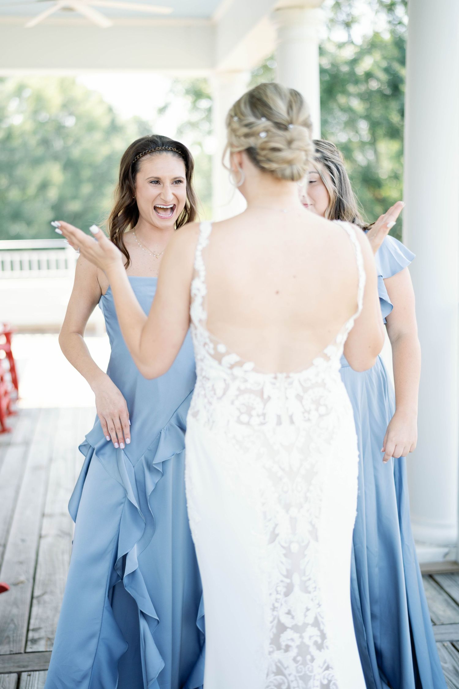 Bridesmaids in light blue dresses share joyful moments with bride in white lace gown during outdoor wedding celebration.
