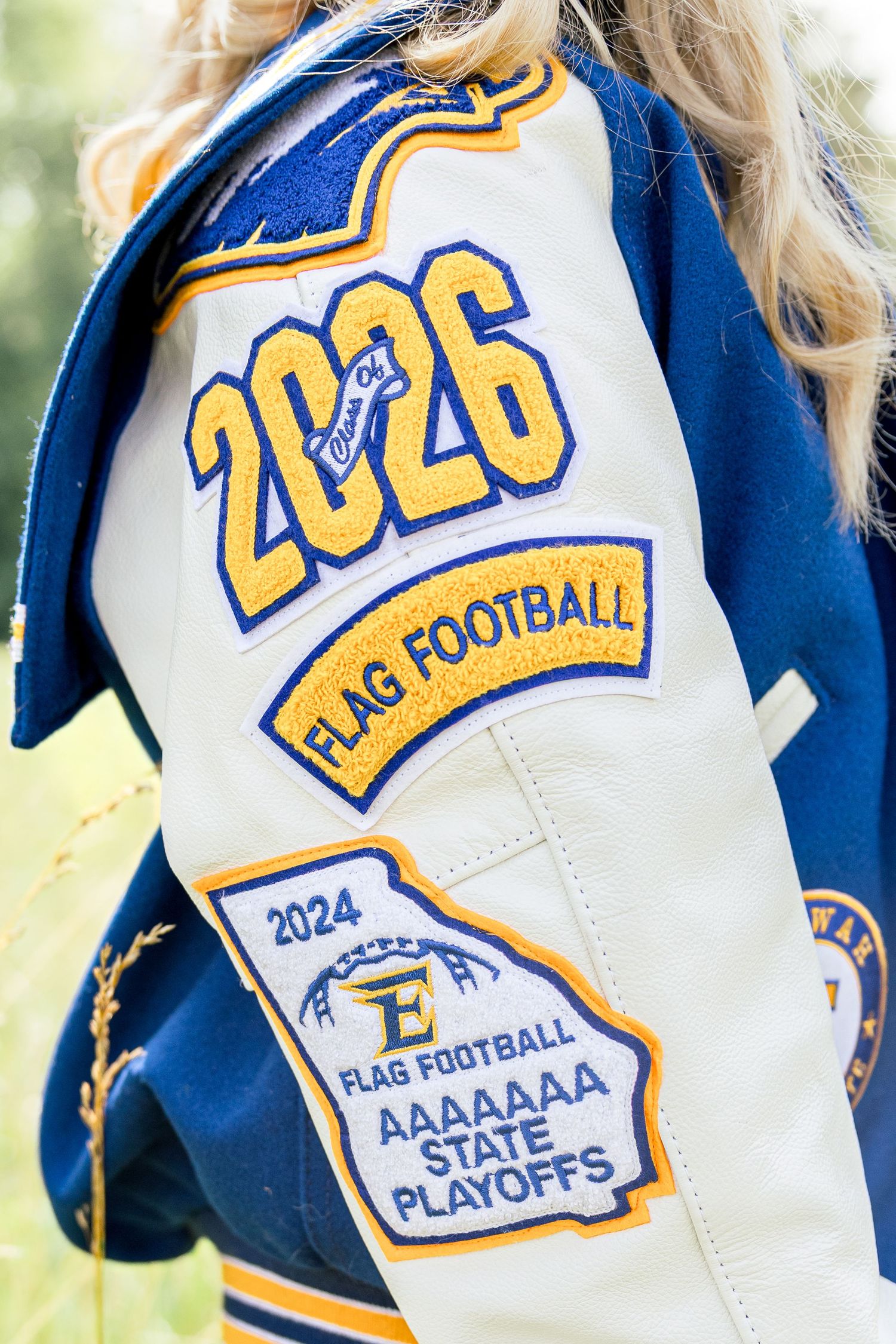 Blue and gold varsity style letterman jackets showing football team logos and state playoff patches.
