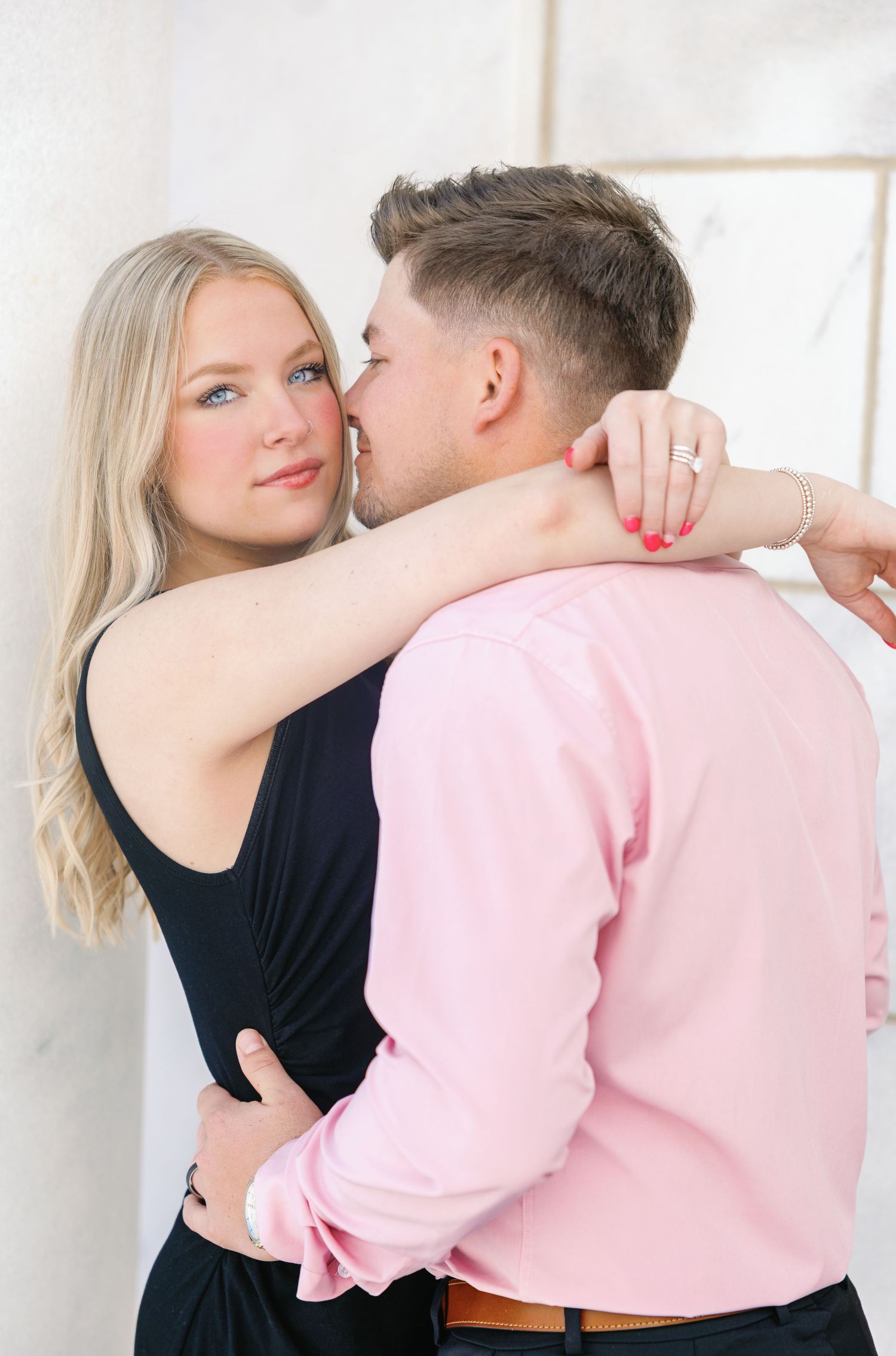 Romantic couple embraces in soft lighting, woman in black dress and man in pink shirt share an intimate moment.