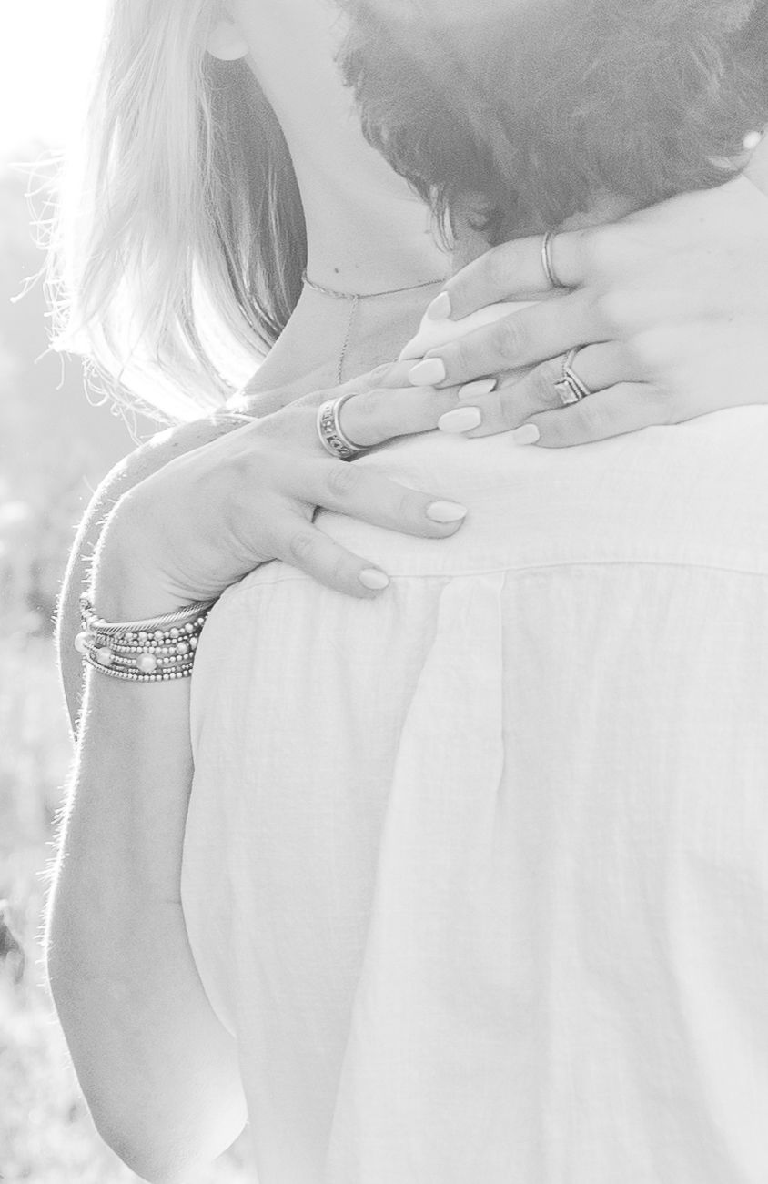 Close-up black and white shot showing hands with rings embracing during an intimate moment.